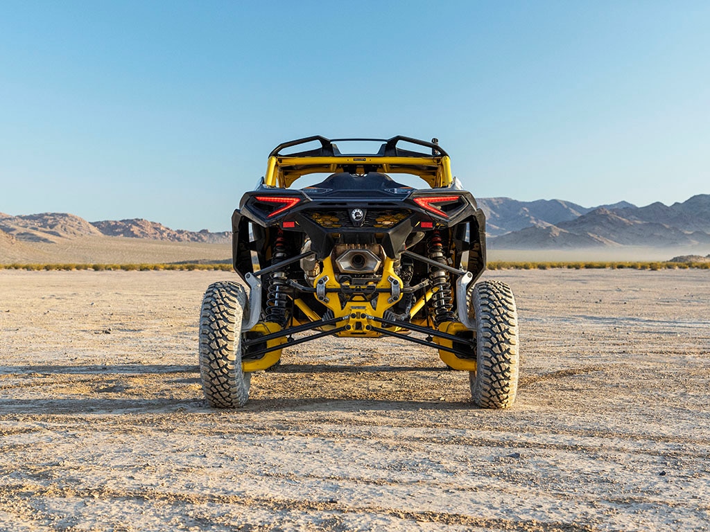 Close-up da extremidade traseira e dos amortecedores de um Can-Am Maverick R estacionado em um deserto.