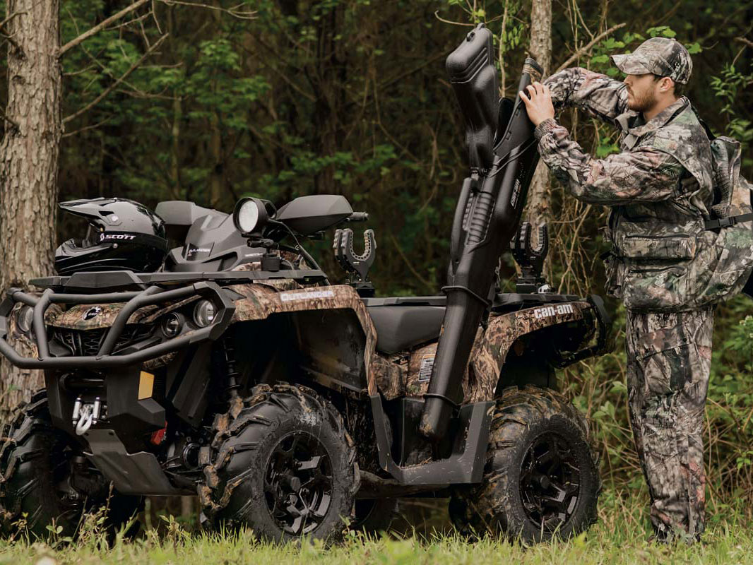 A man storing his rifle next to his Can-Am Oulander Mossy Oak Edition ATV while hunting