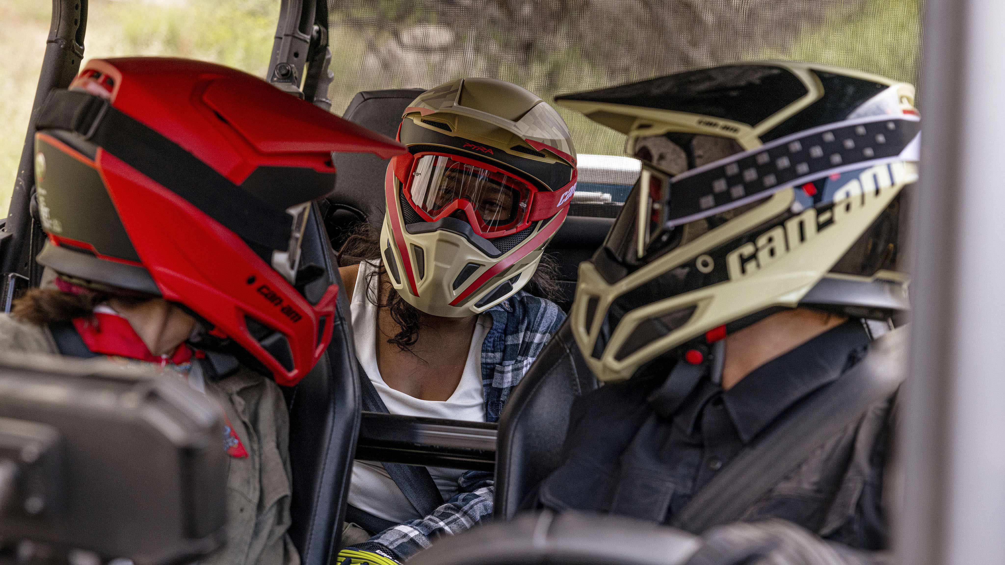 Three riders sitting in a Can-Am Off-Road vehicles wearing safety helmets