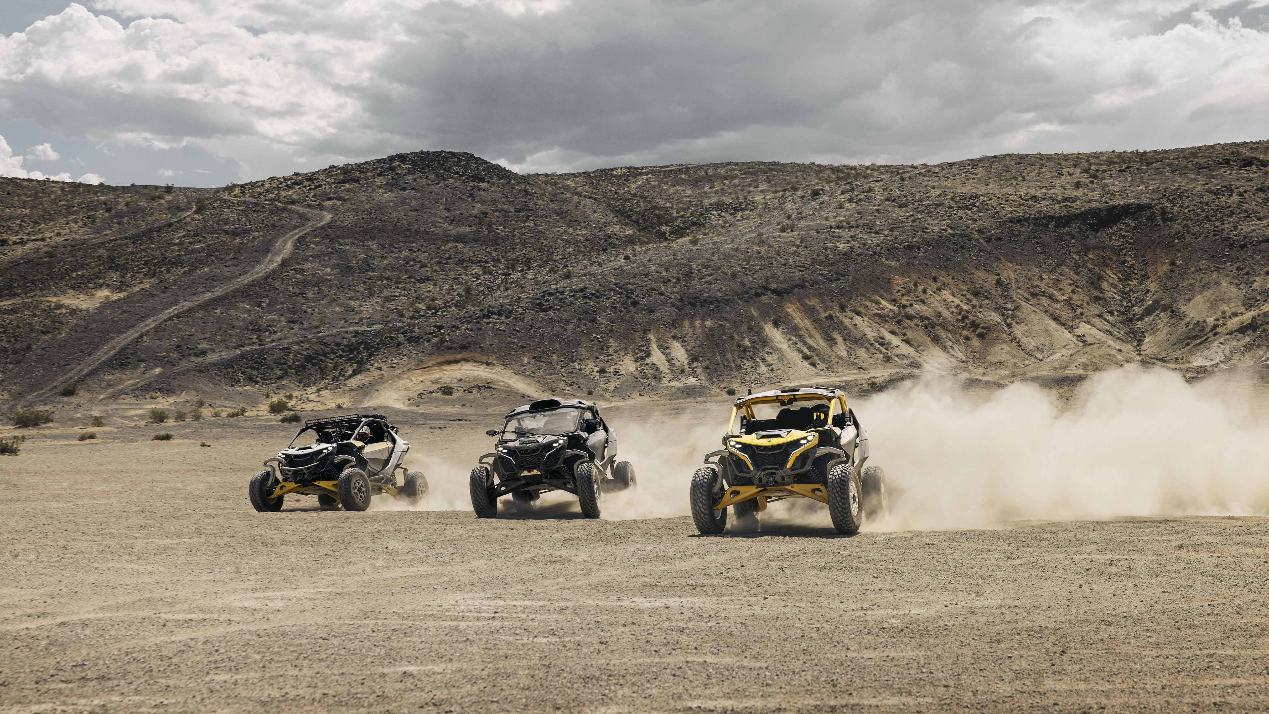 Three Can-Am Maverick R SxS vehicles racing through the desert