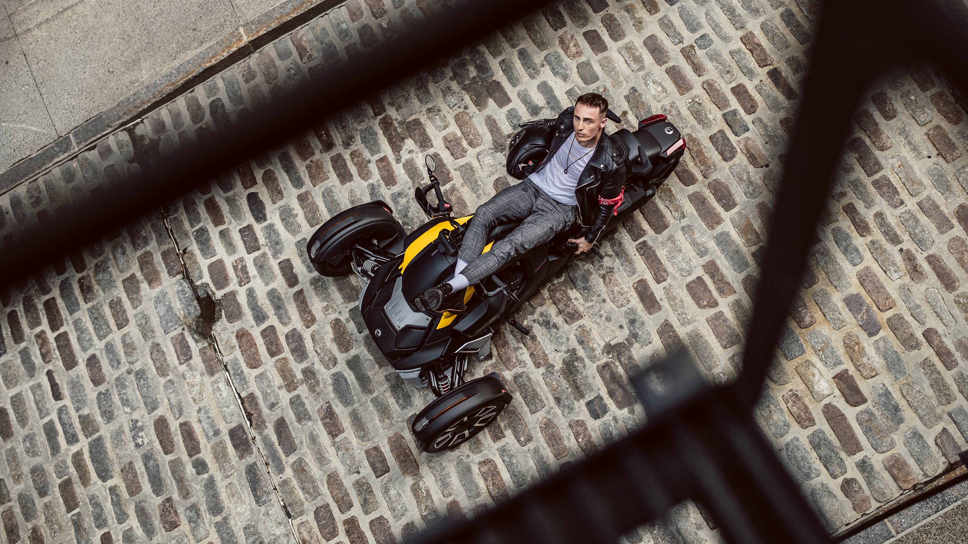 A man reclining on his Can-Am vehicle, which is parked in a cobblestone alleyway