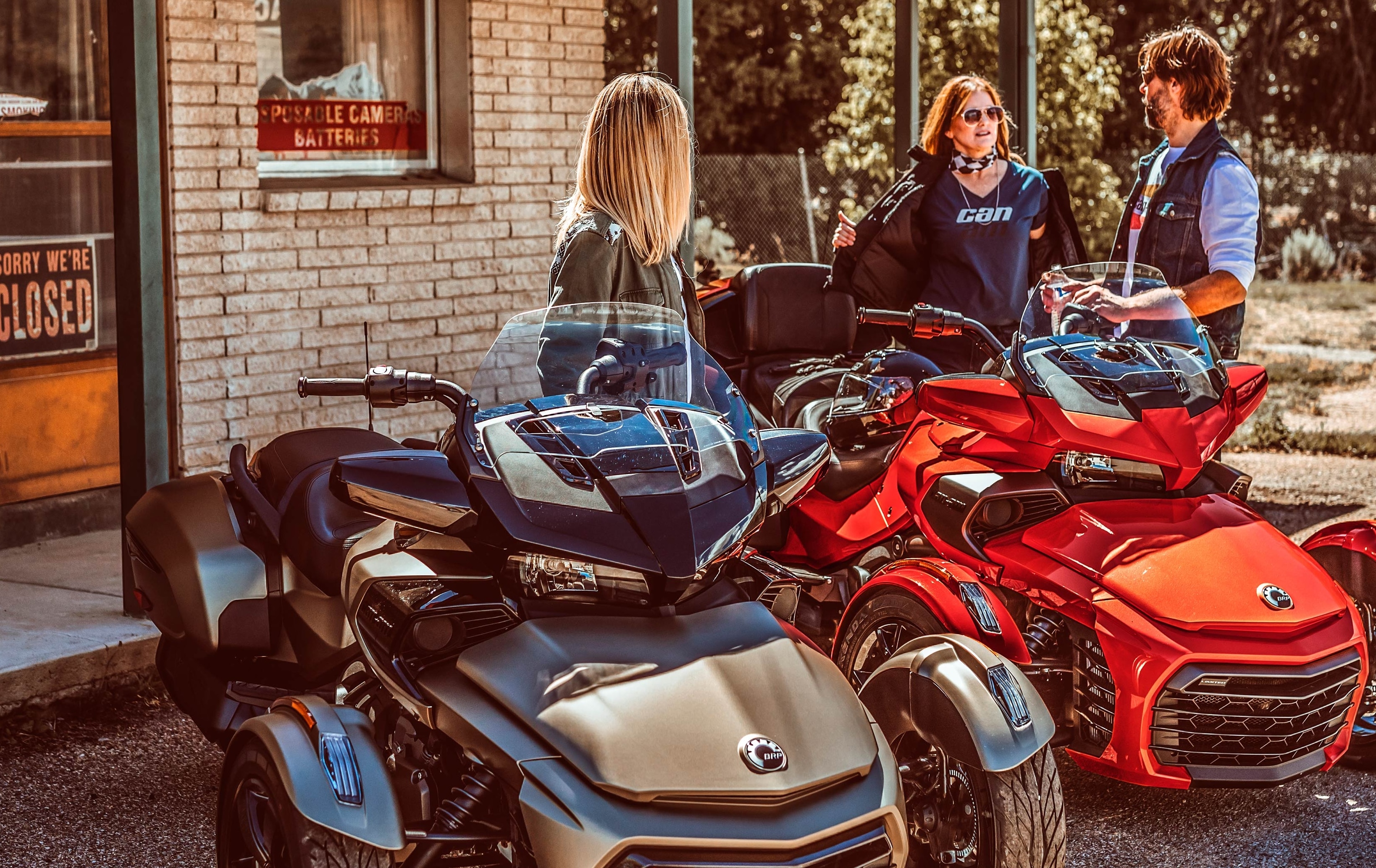 Three friends chatting by two Can-Am Spyder vehicles parked in front of a general store