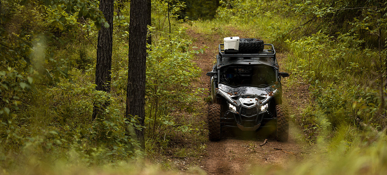 Two riders on a Can-Am Maverick Trail side-by-side on a lush green mountain trail