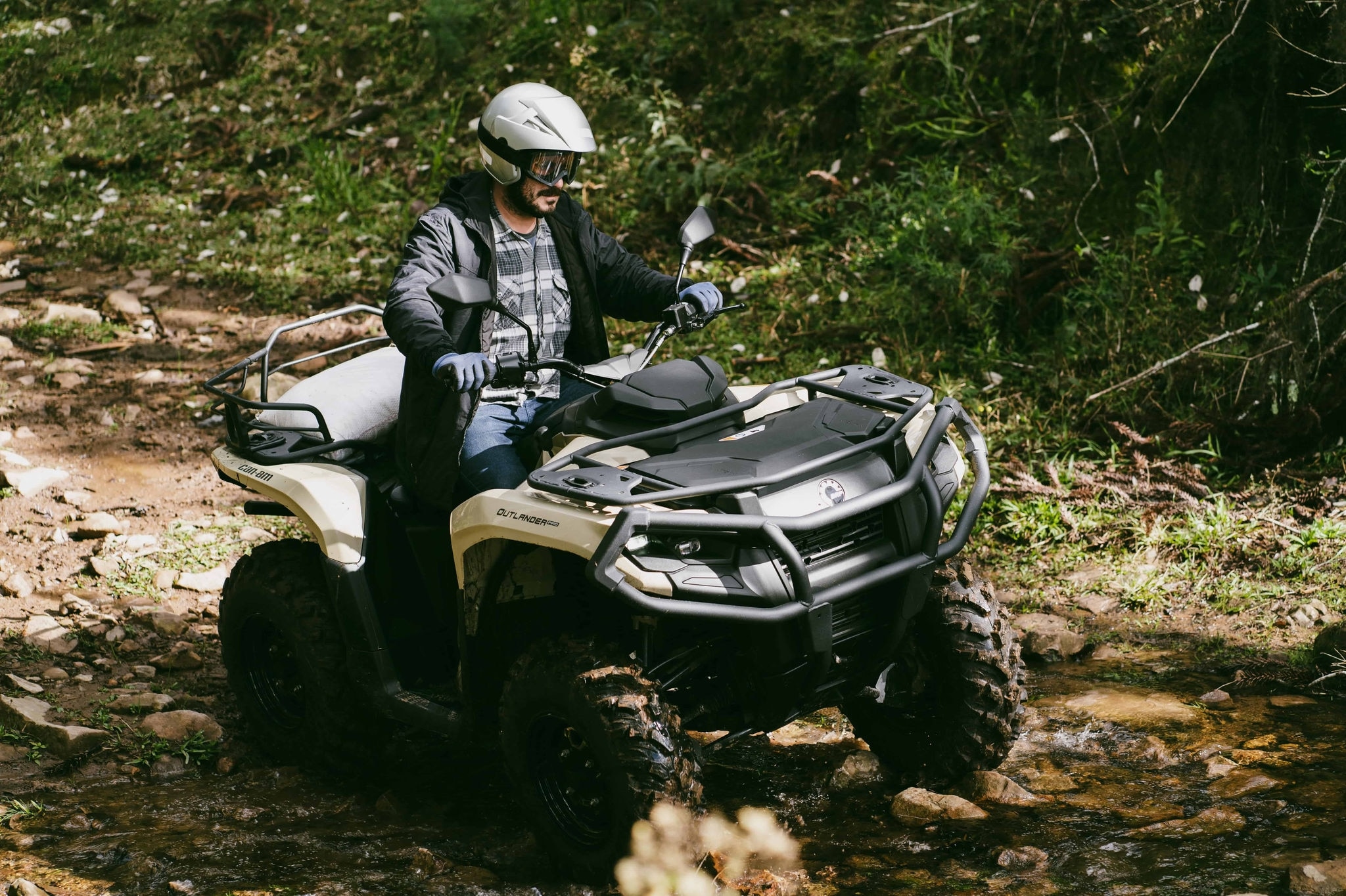 Can-Am Outlander Pro em ação em terreno rochoso e enlameado.