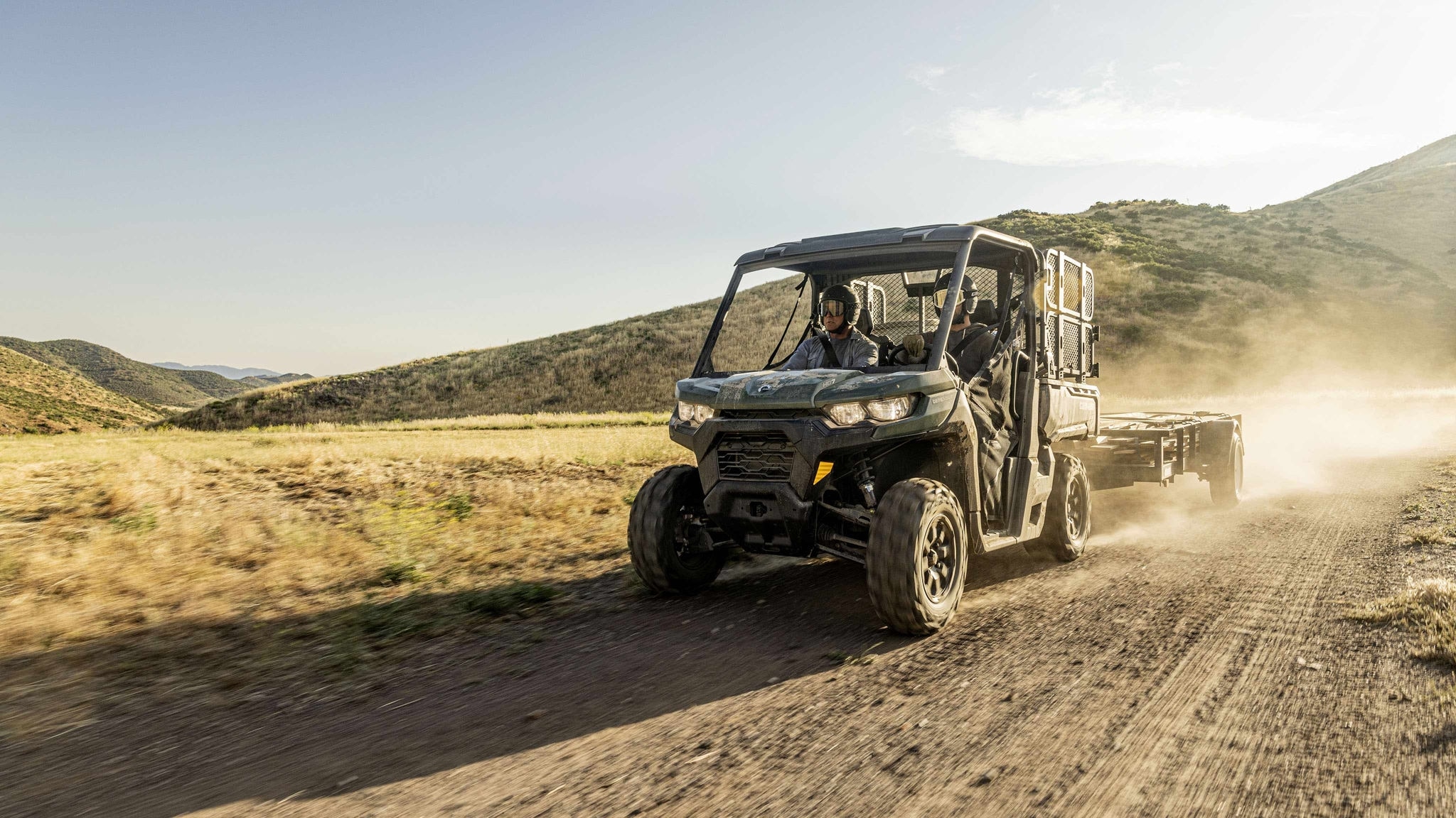 Pilotos a bordo de um Can-Am Defender em movimento em estrada de terra.