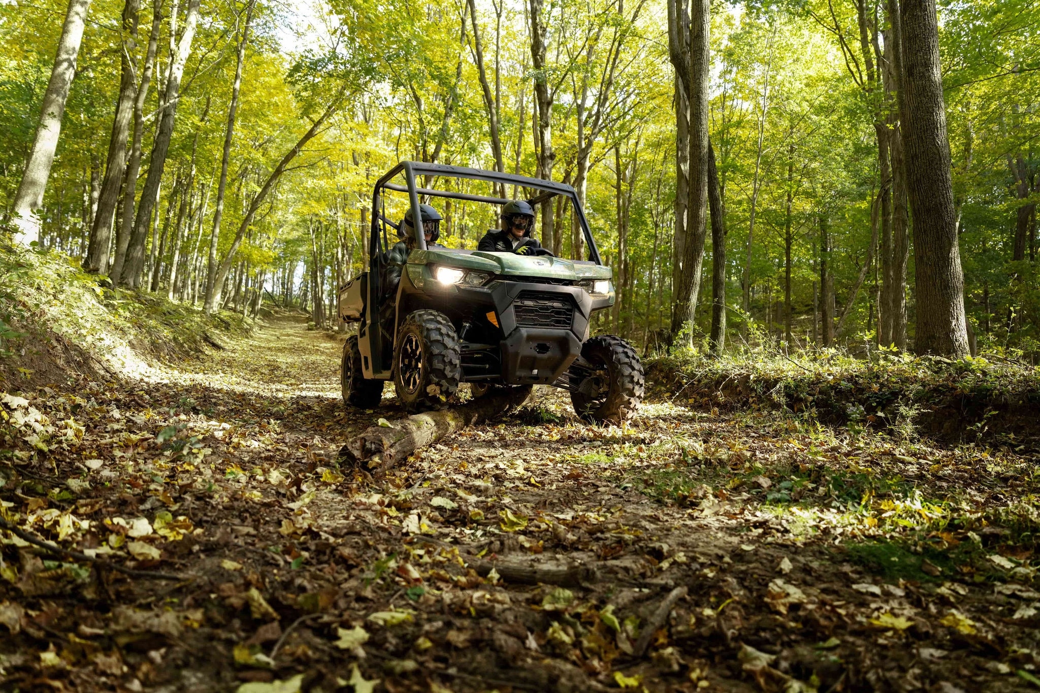 Can-Am Defender em movimento em trilha com folhas e galhos pelo caminho.
