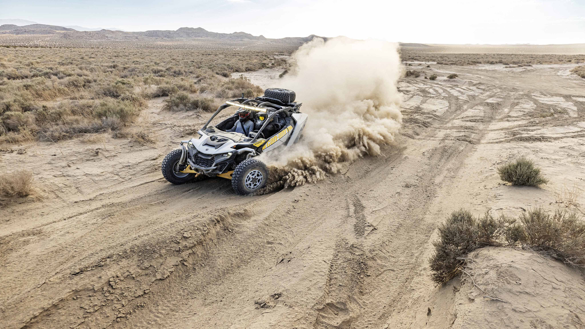 Close-up of a rider in a Can-Am Maverick R climbing a dune in the desert