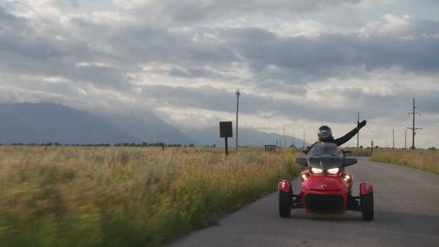 Can-AM 3-wheeled vehicle on a road passing in front of a gas station 