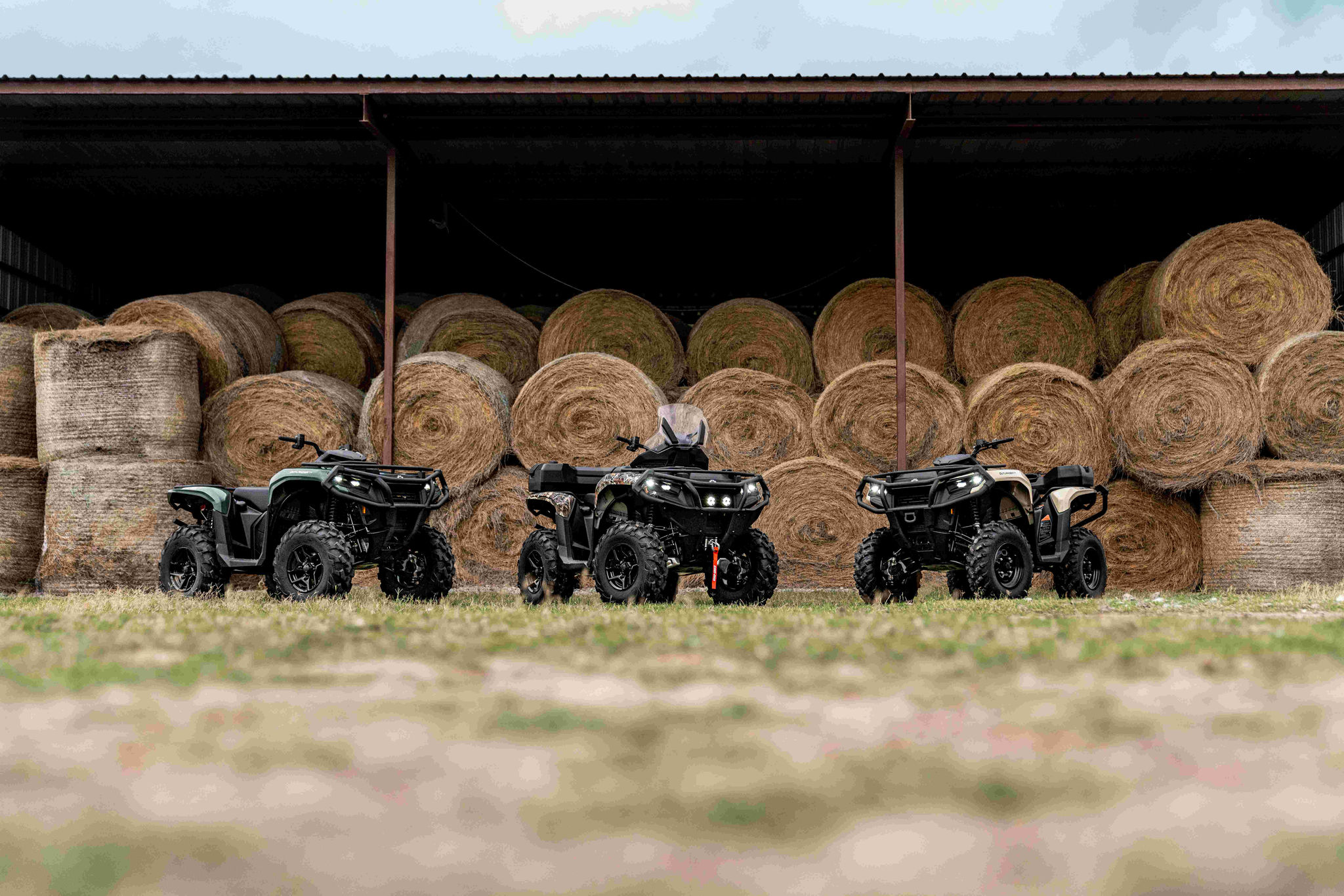 3 Can-Am Outlander Pro vor einer Scheune geparkt.
