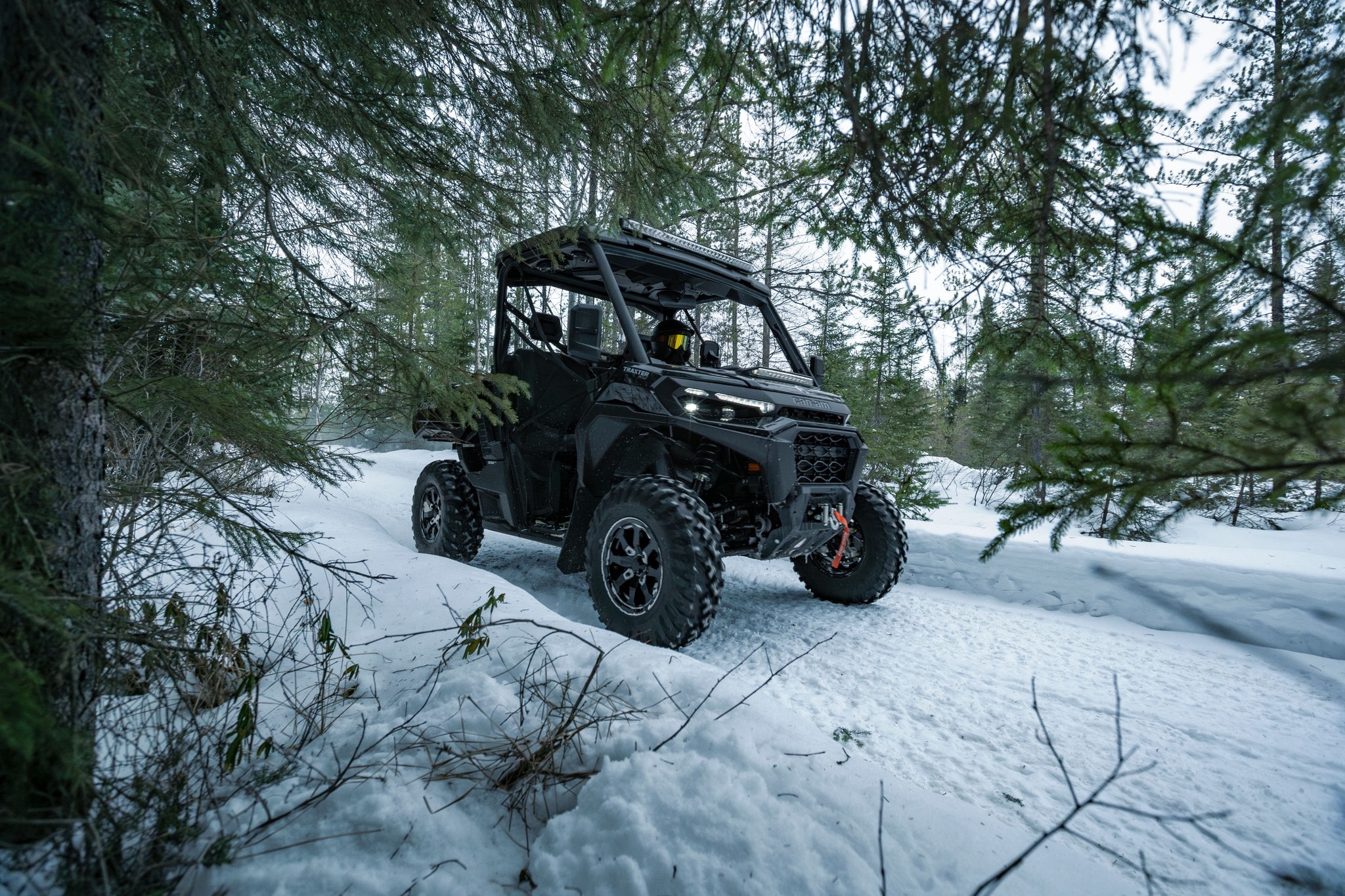 Un Can-Am Traxter XU HD11 parcourant un chemin enneigé à travers la forêt