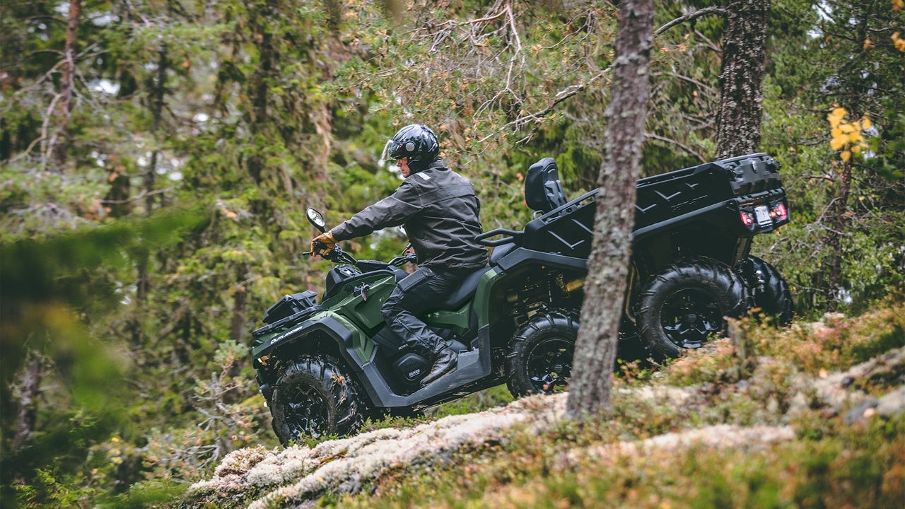 Un piloto conduciendo su Can-Am Outlander 6x6 verde boreal por una colina