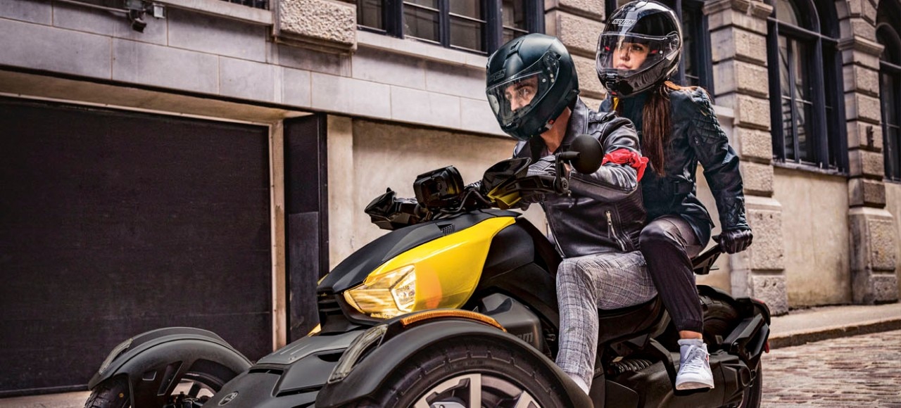 Couple riding on a Ryker with yellow panels through the city streets.
