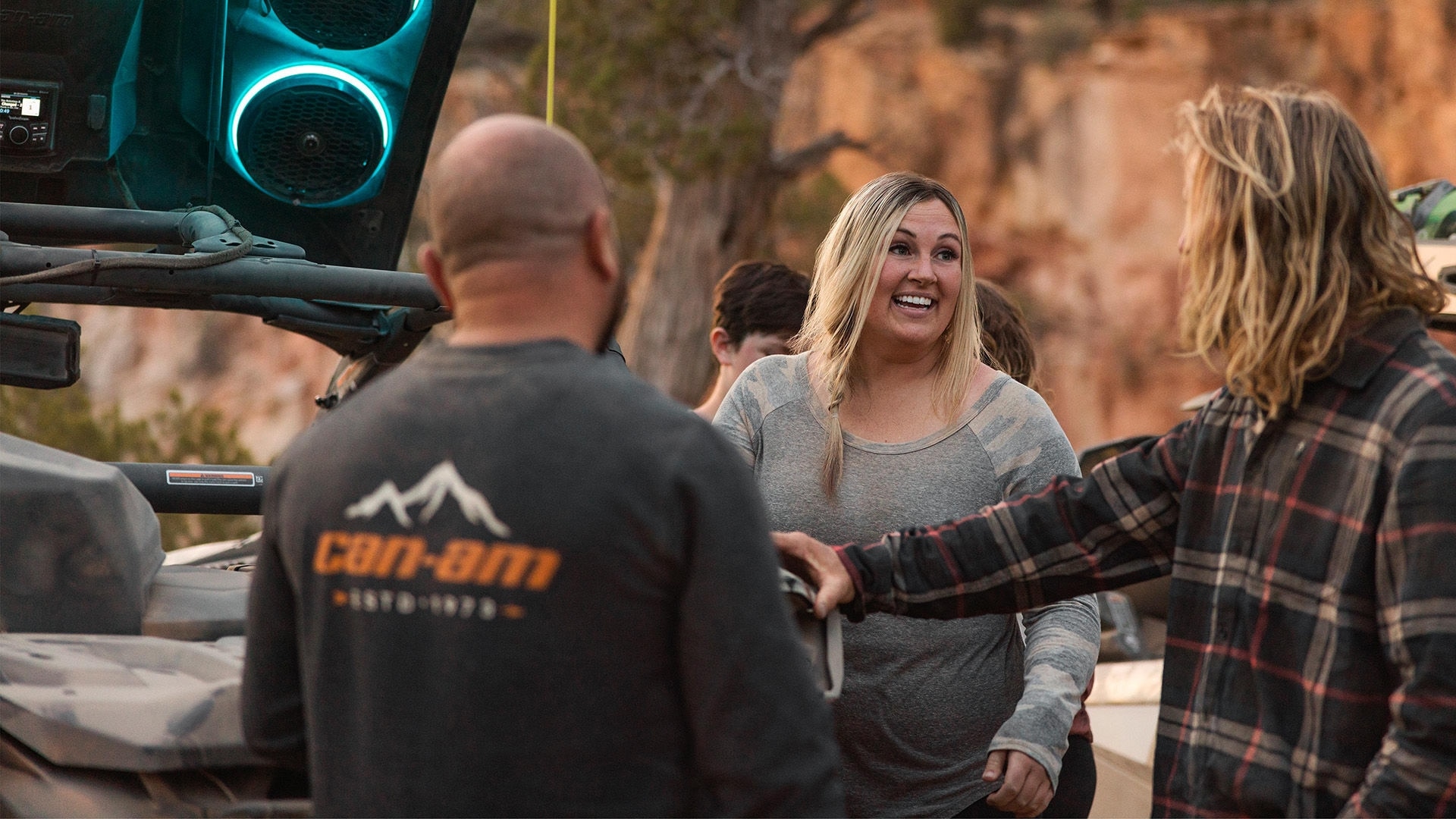 Can-Am riders speaking to each other next to a Can-Am Maverick X3 equipped with an audio roof