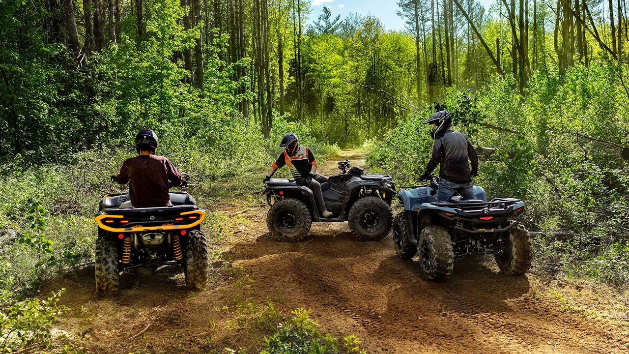 Plusieurs VTT Can-Am Outlander 2026 sur un chemin de terre en forêt