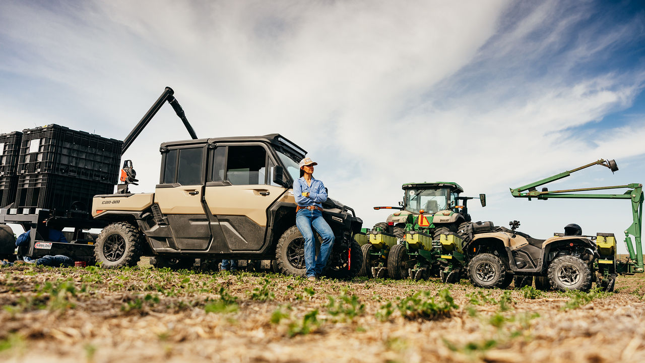 Une femme assise à côté de son Can-Am Defender XU HD10/HD11, près d'autres véhicules utilitaires