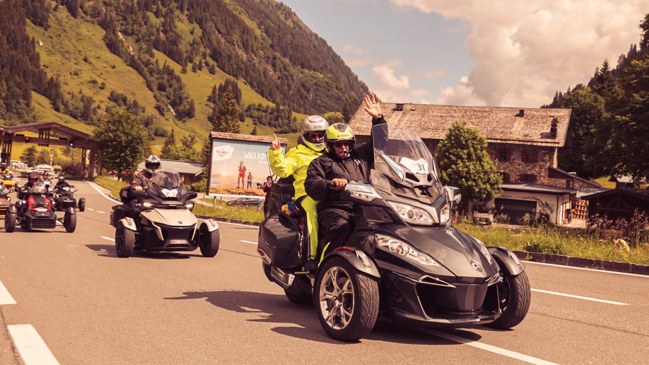 A group of riders driving Can-Am 3-wheeled vehicles on a paved road