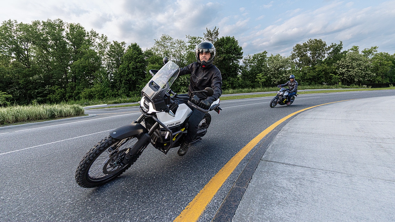 Two 2026 Can-Am Electric Motorcycles taking a curve on a paved road