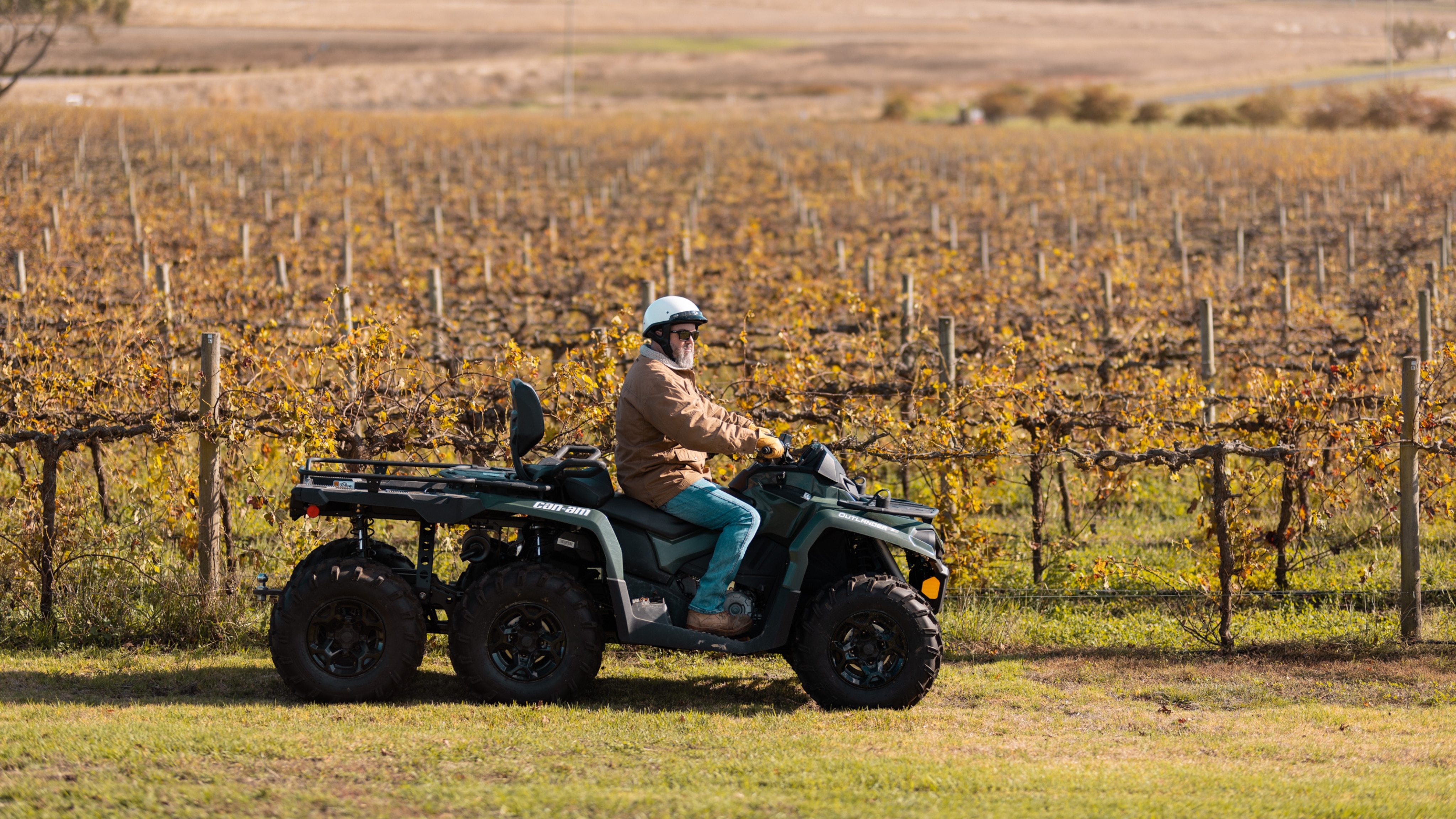 man driving outlander 6x6 through a vineyard