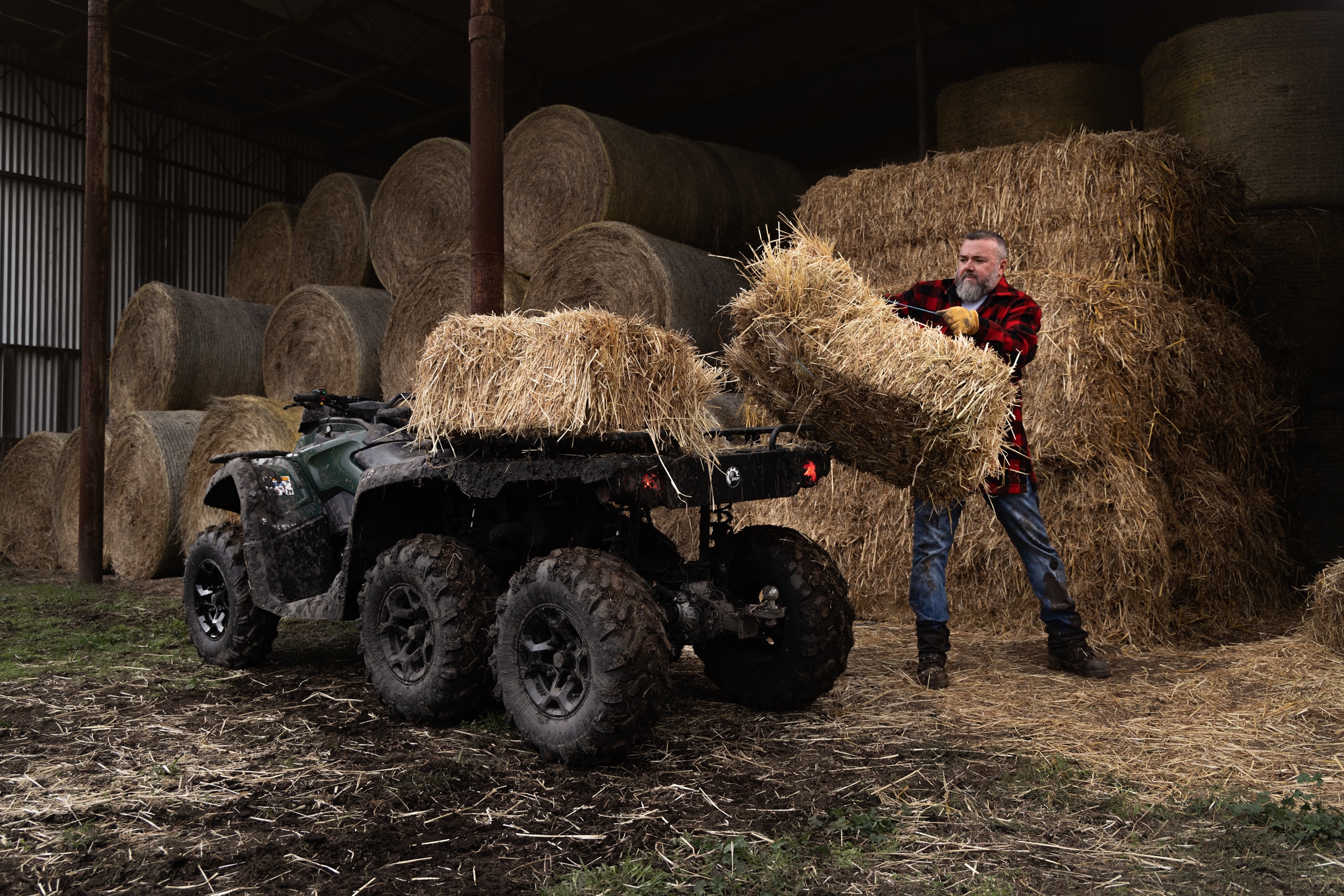 Farmer throuwing hay bales onto the back of an outlander 6x6