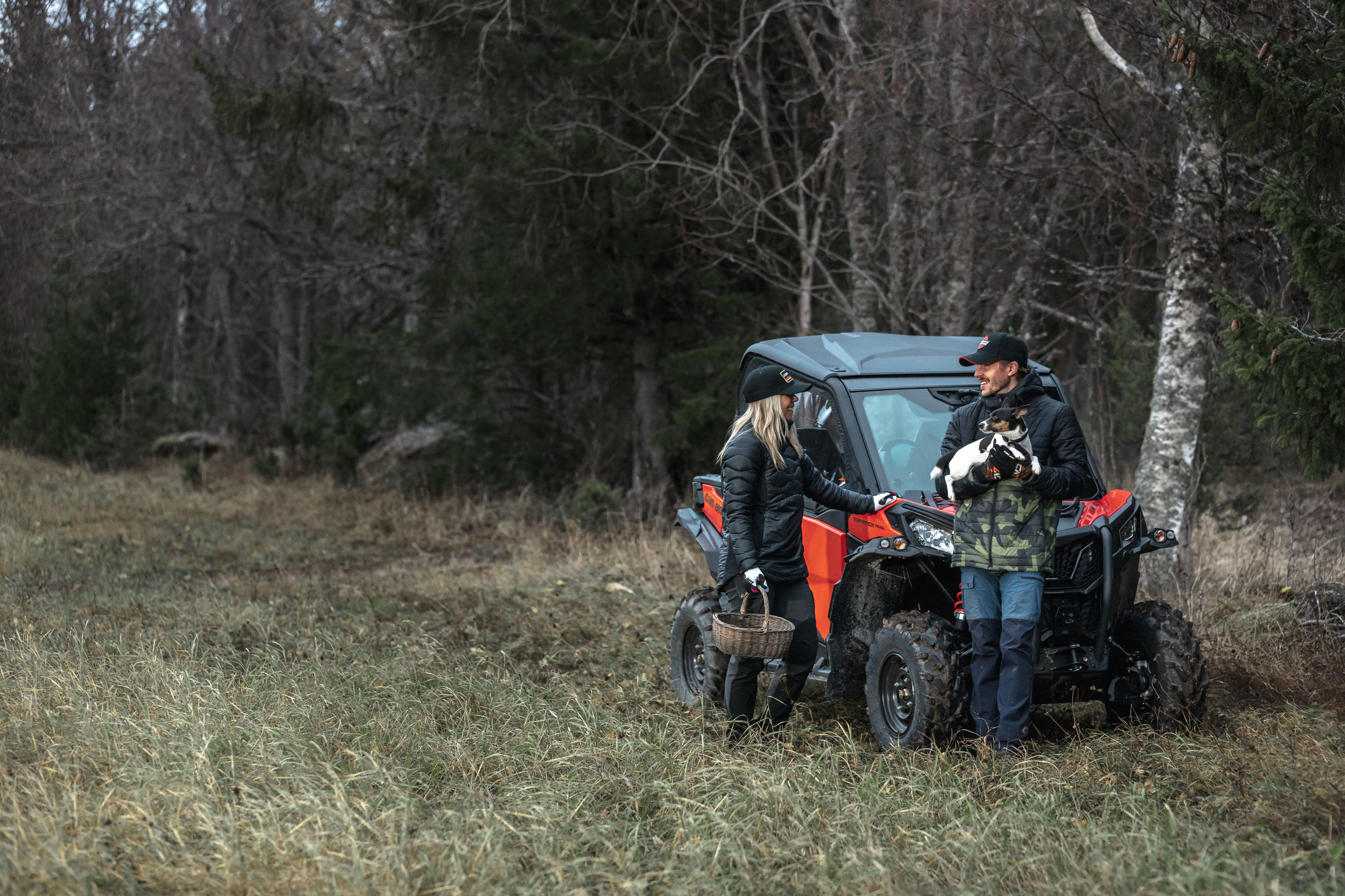 Two riders outside their Can-Am Maverick Trail 800 on an adventure with their puppy
