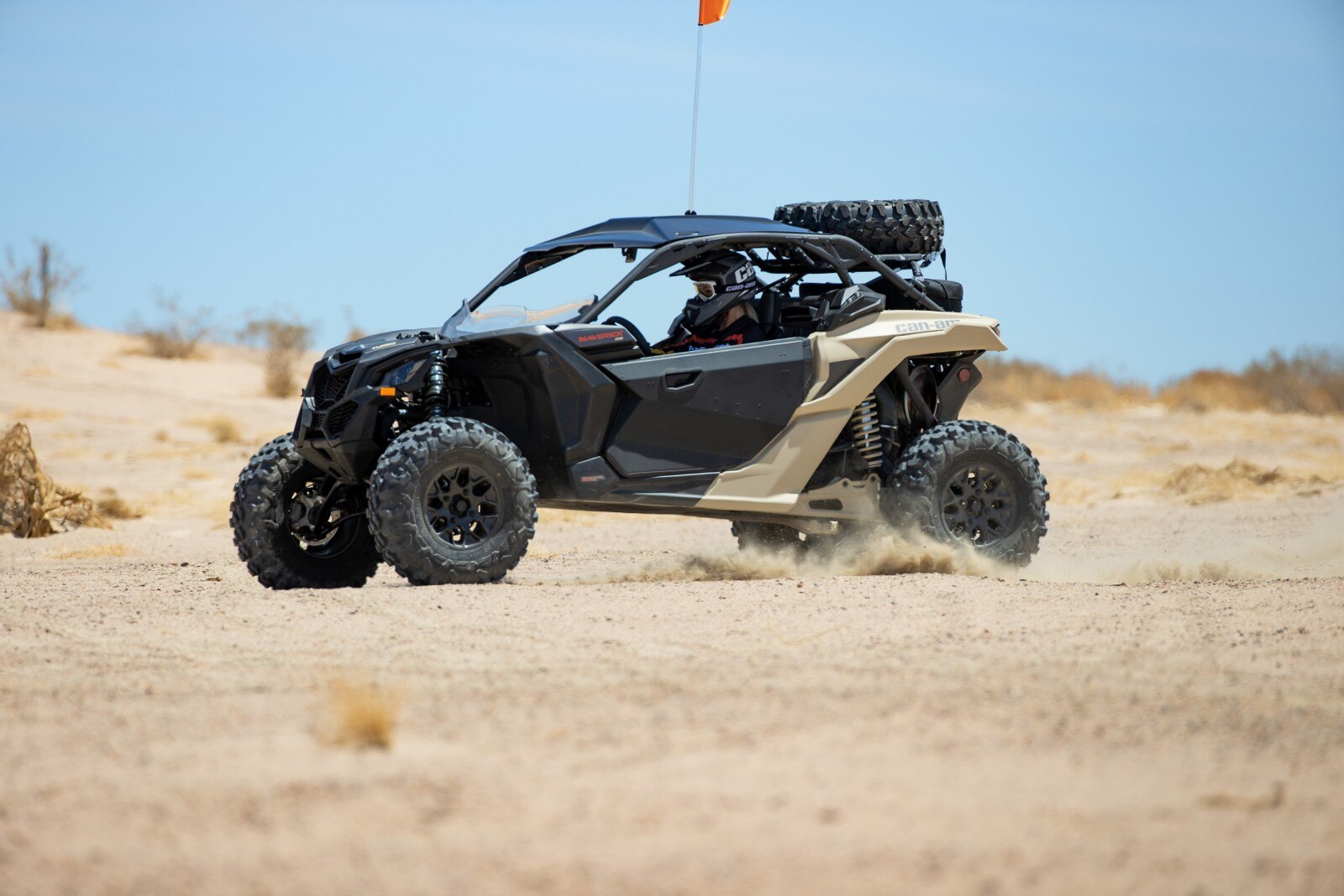 A driver wearing a Pyra helmet in a desert tan Can-Am Maverick driving in a desert setting