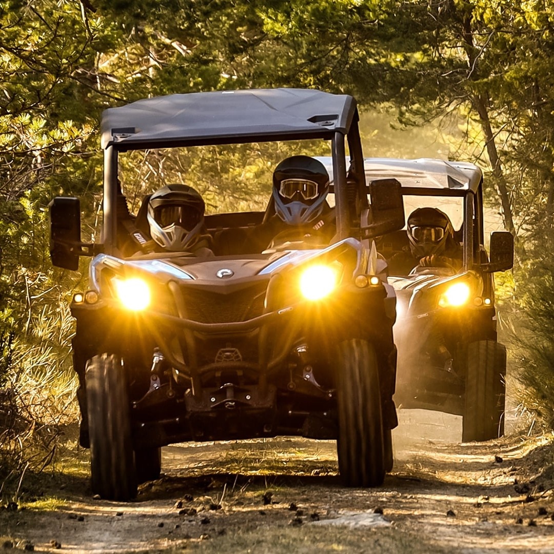 Zwei Can-Am SxS-Fahrzeuge fahren auf einem von Bäumen umgebenen Feldweg