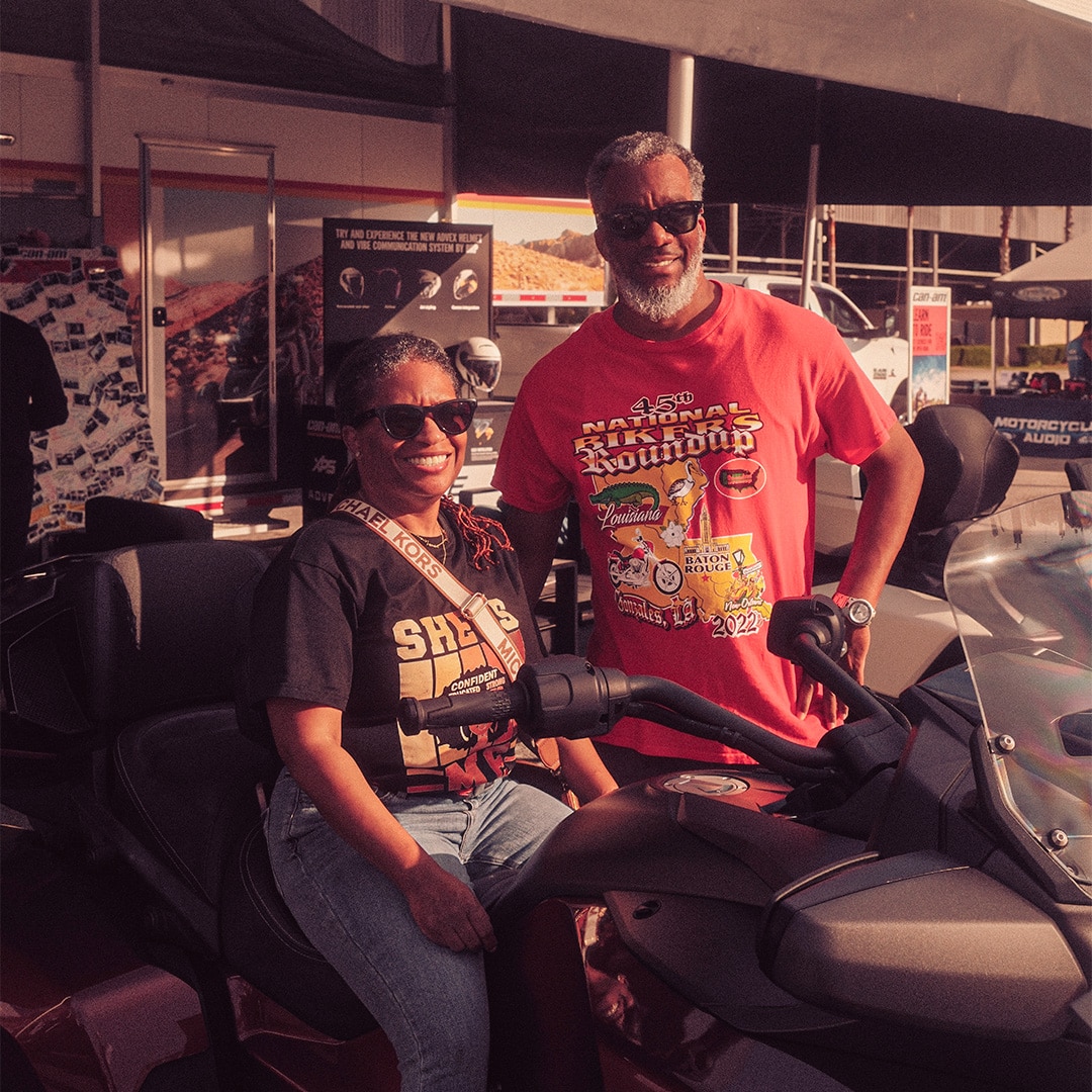 A smiling couple standing next to their 3-wheel