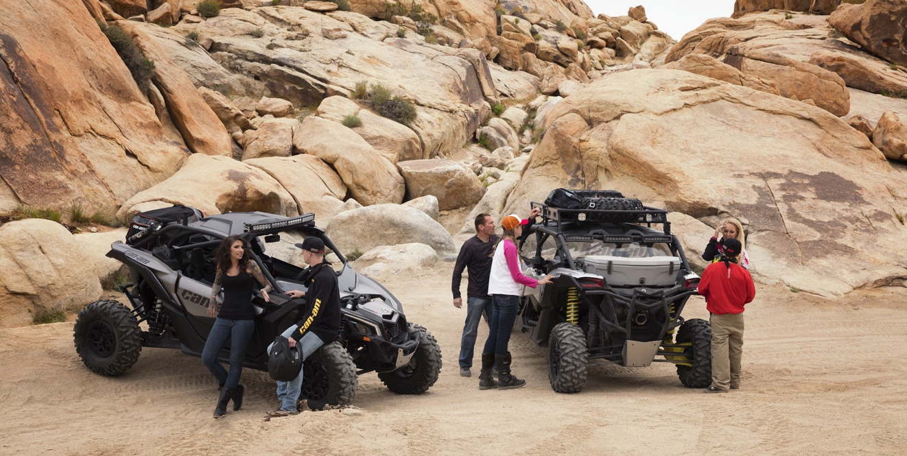 A bunch of people talking in the desert beside three 4-seater Can-Am Maverick X3 MAX side-by-side