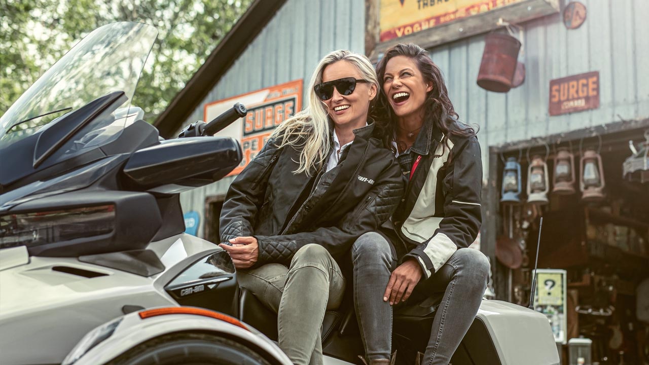 Two girls sitting and smiling on a Spyder.