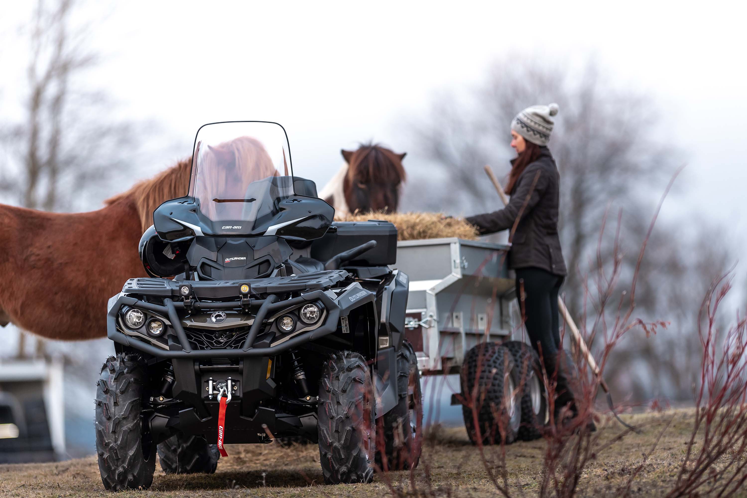 A Platinum Satin Outlander MAX 1000R towing a trailer full of hay as a farmer feeds her horses. 