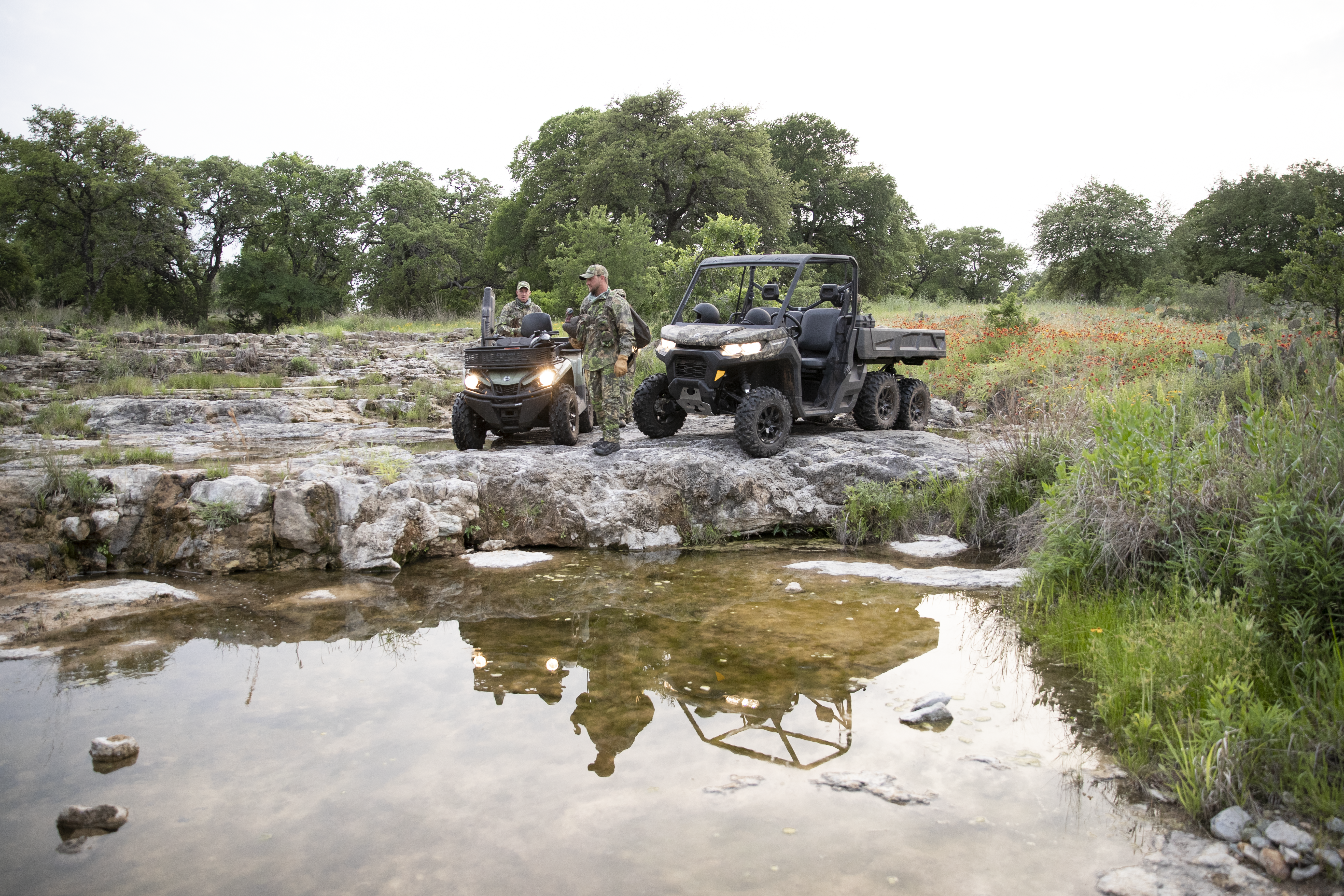 Two hunters near the water next to a custom hunting Can-Am Defender side-by-side