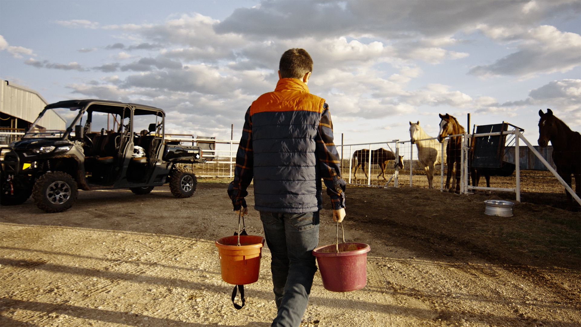 Young rancher carrying buckets near a Can-Am Defender