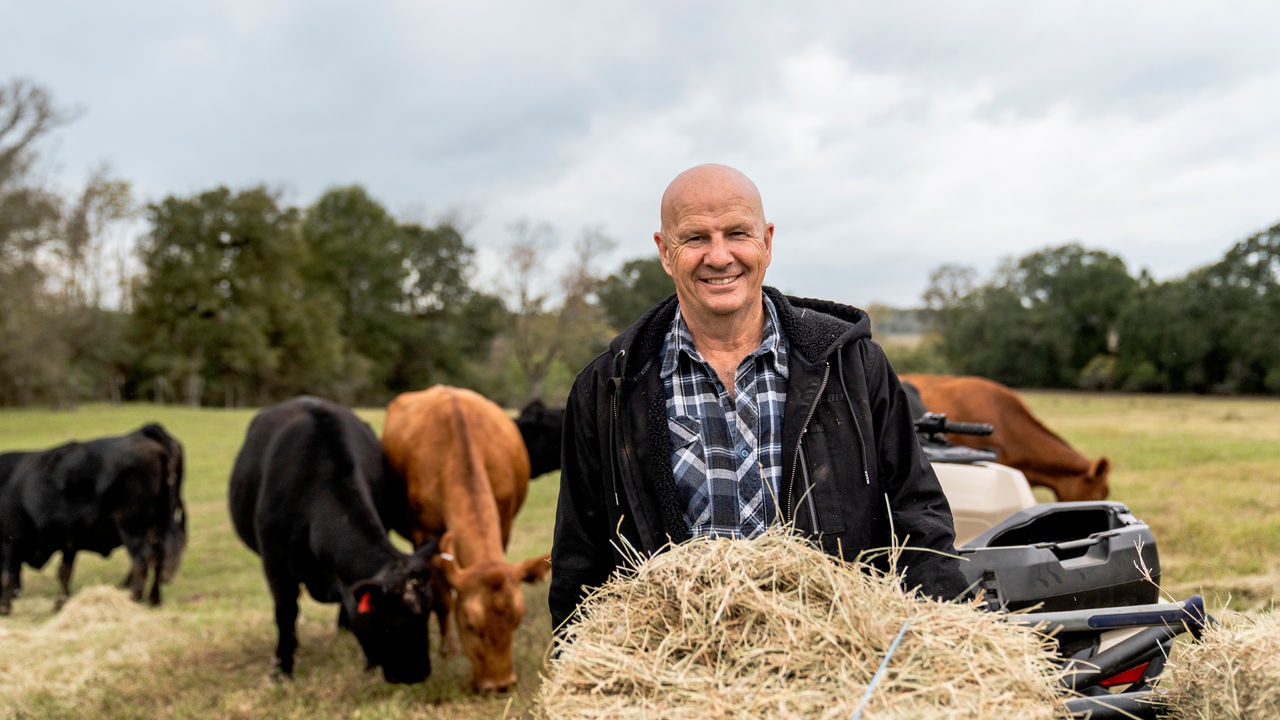 Maanviljelijä antaa heinää karjalleen 2023 Outlander PRO ATV:n vieressä