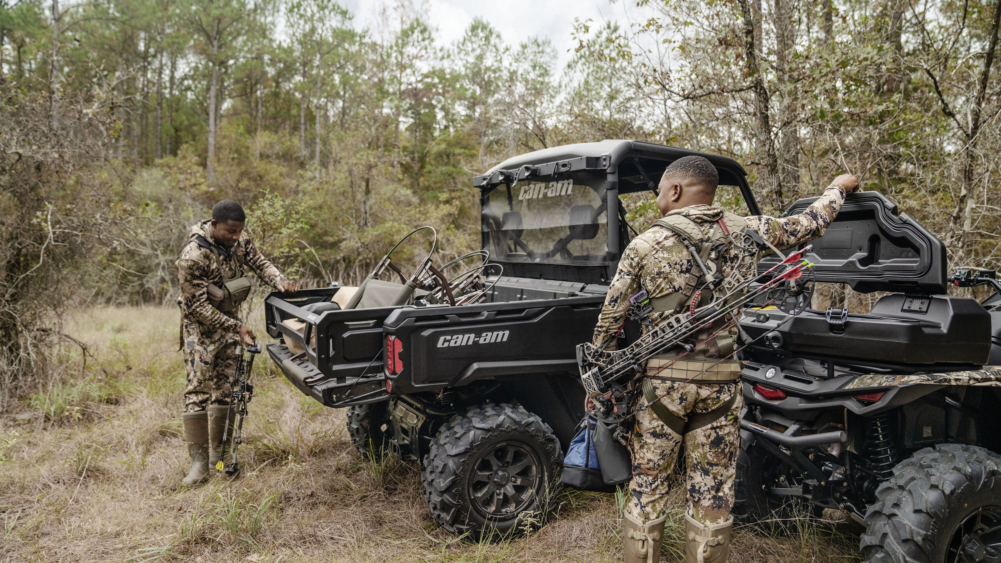 Two hunters getting geared up near their Can-Am Defender and Outlander PRO Hunting Edition