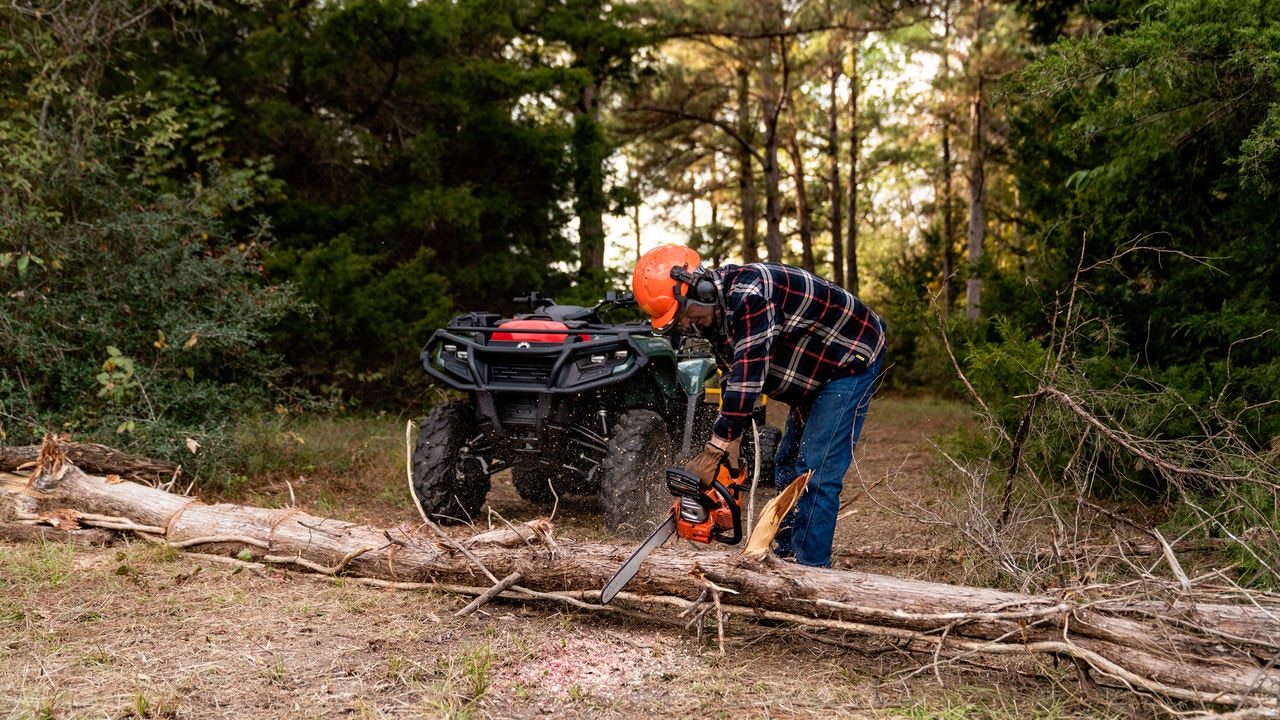 A man uses a chainsaw in front of a Can-Am ATV