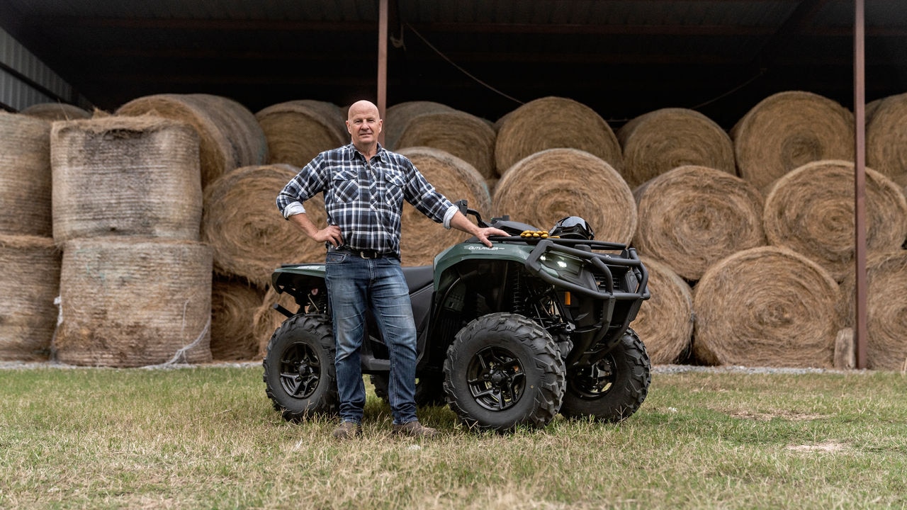 A farmer standing next to his Tundra Green Outlander PRO XU in front of several stacked round hay bales