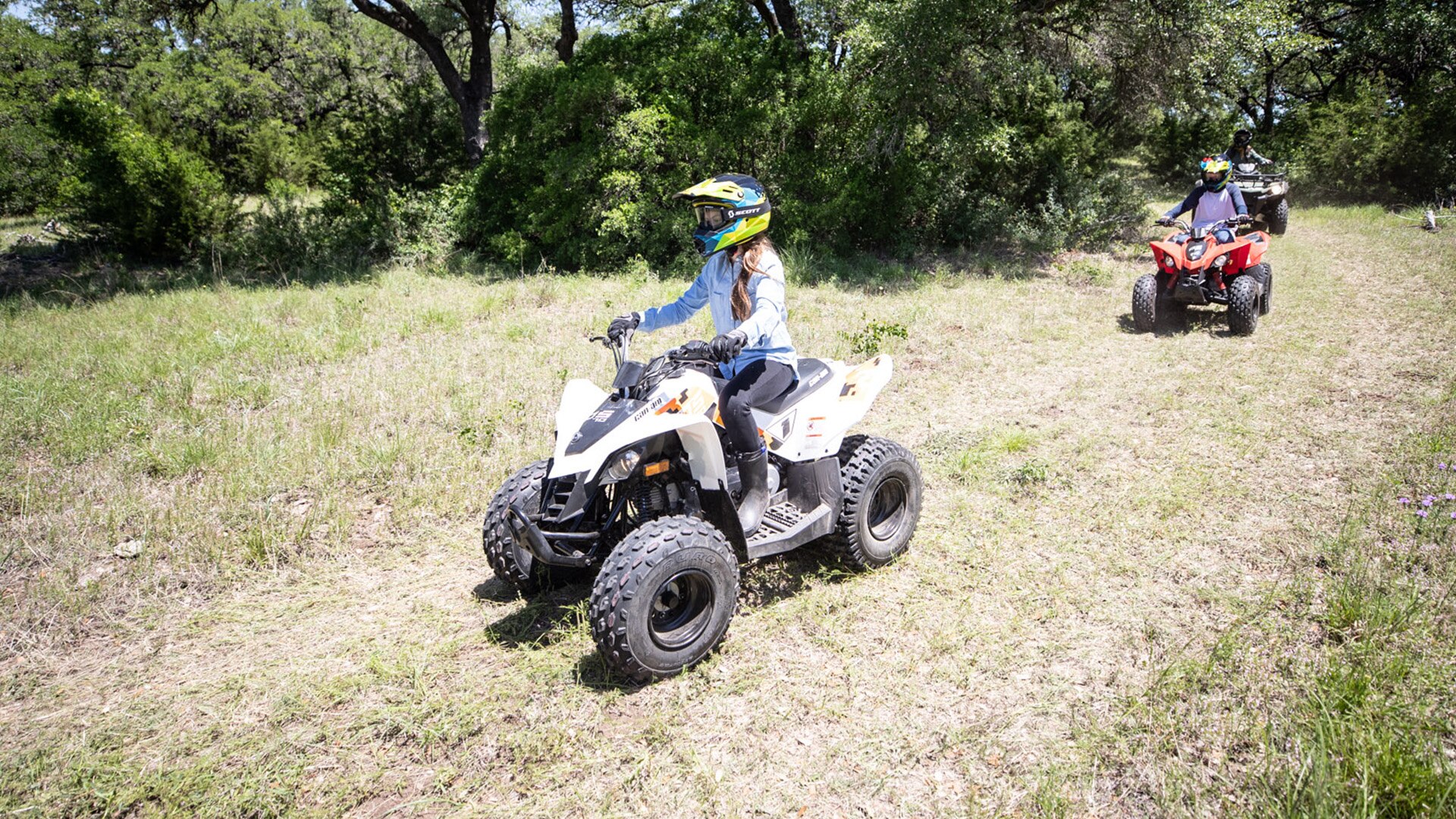 Young girl riding a Can-Am DS ATV followed by her family