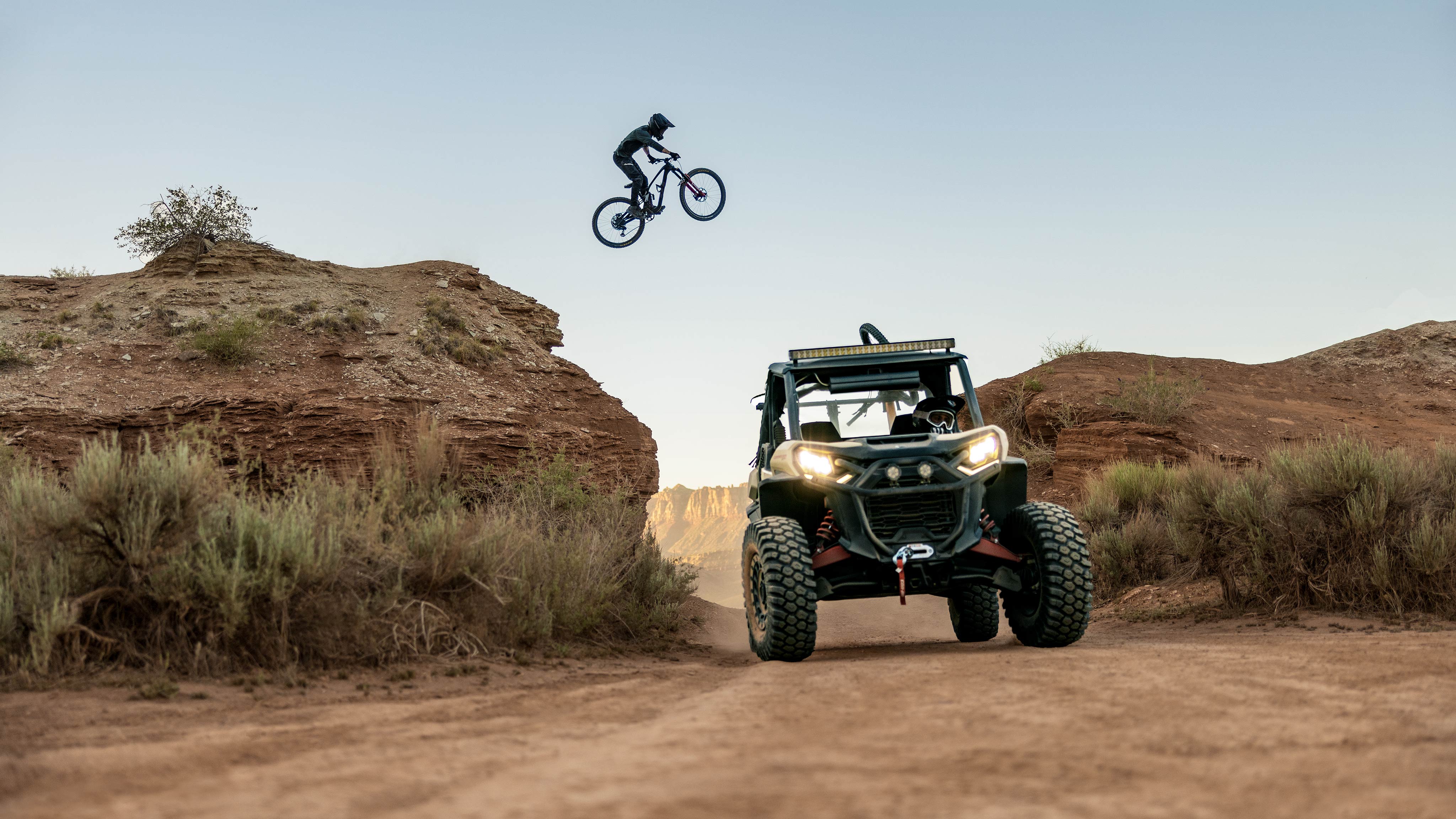 A mountain biker jumping over a Desert Tan & Carbon Black Can-Am Commander XT-P