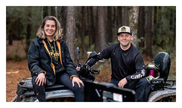 Two persons wearing Can-Am apparel sitting on a 2024 Outlander