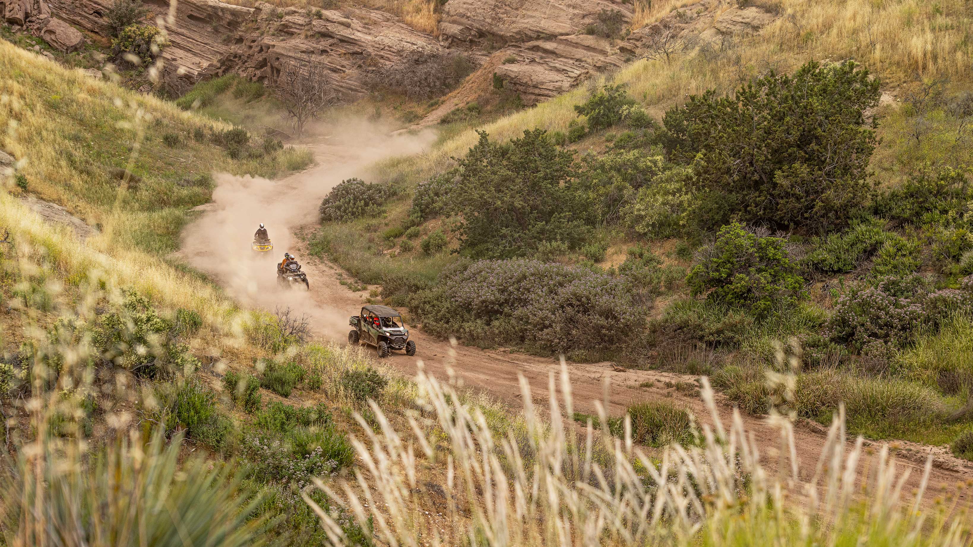 A Can-Am Side-by-Side, followed by two ATVs on an unpaved road