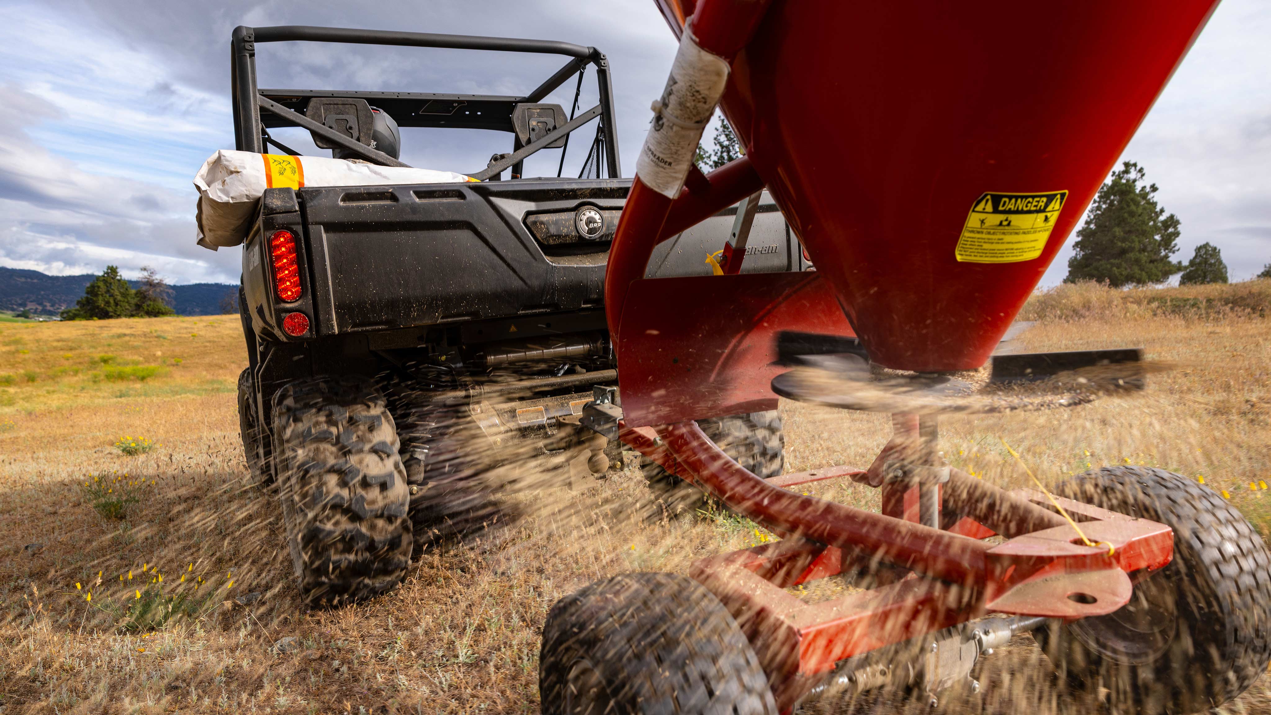 Vy över en spannmålsdistributör fäst bakom en Can-Am Defender 2025 utformad för gården