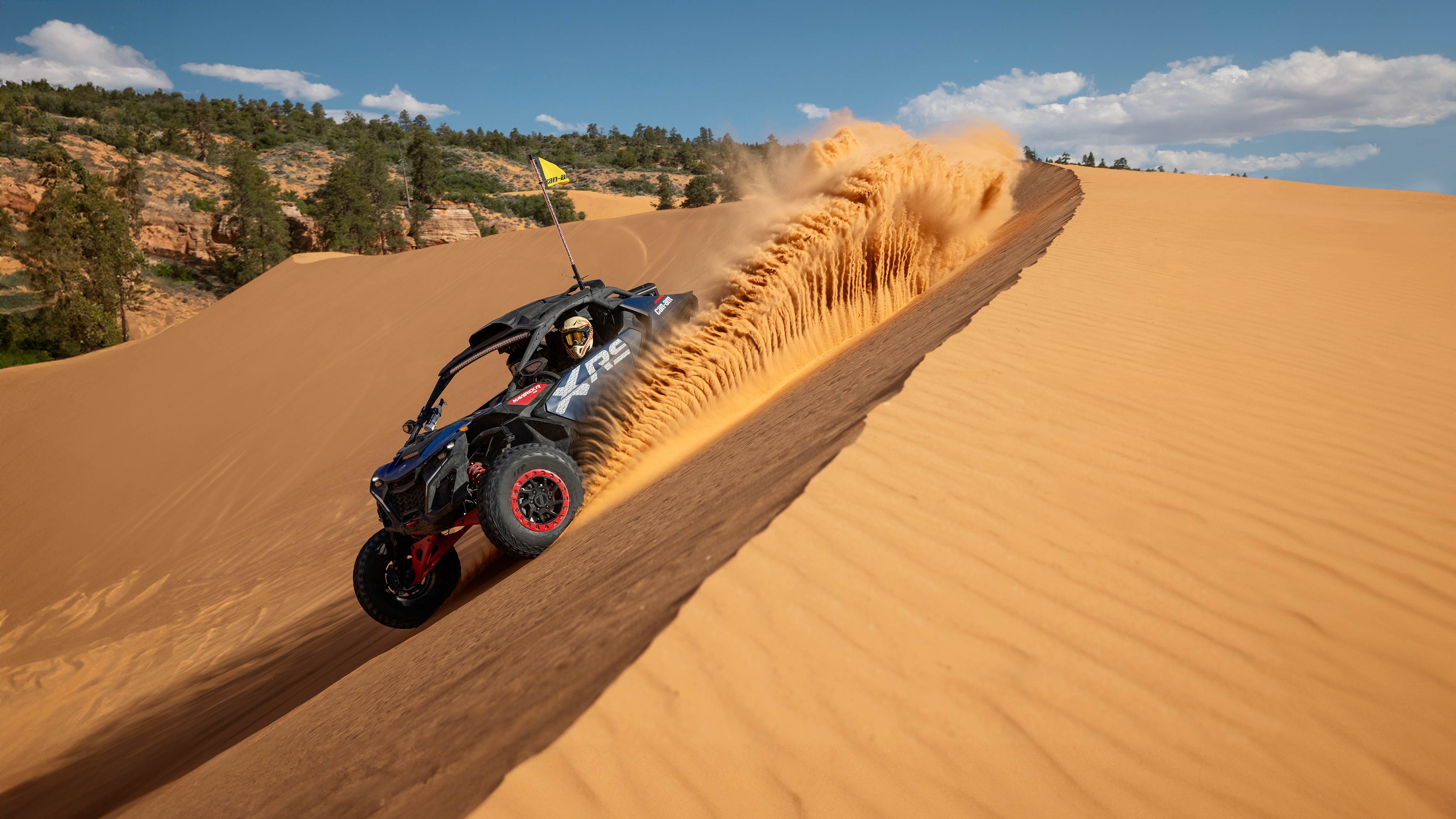 Un Can-Am Maverick R X RS 2025 rodando por una duna de arena en un día soleado