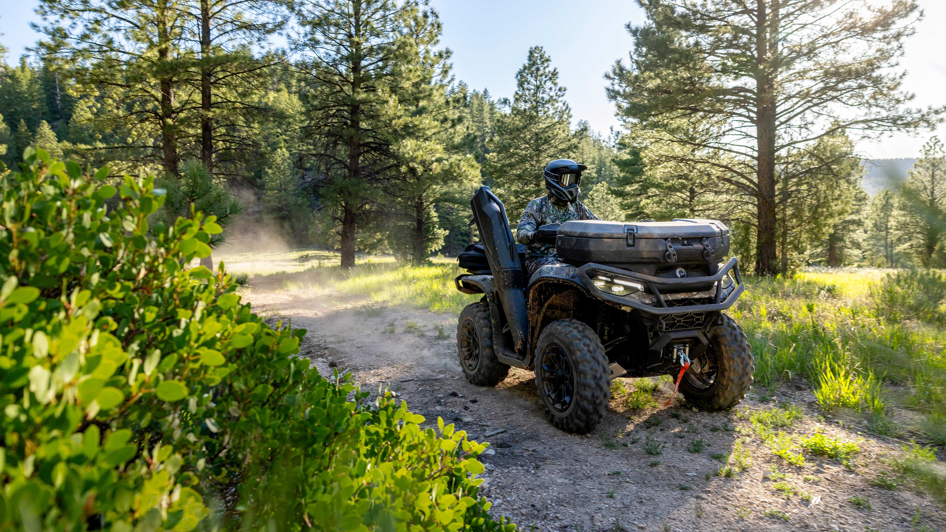 A rider driving a Can-Am Outlander ATV on a dirt trail