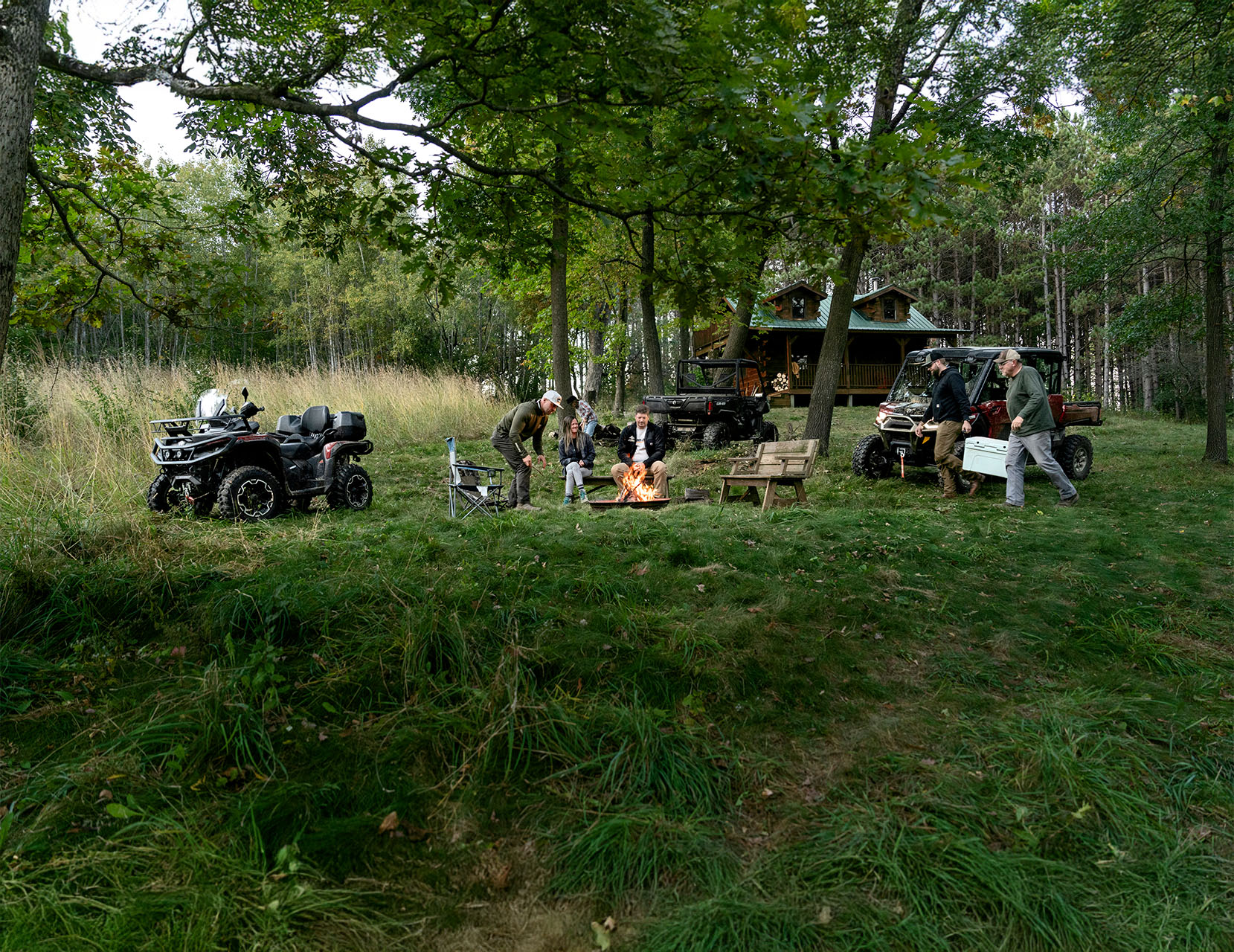 Un groupe de personnes réunies autour d'un feu près d'un chalet avec un VTT et VCC stationnés à proximité