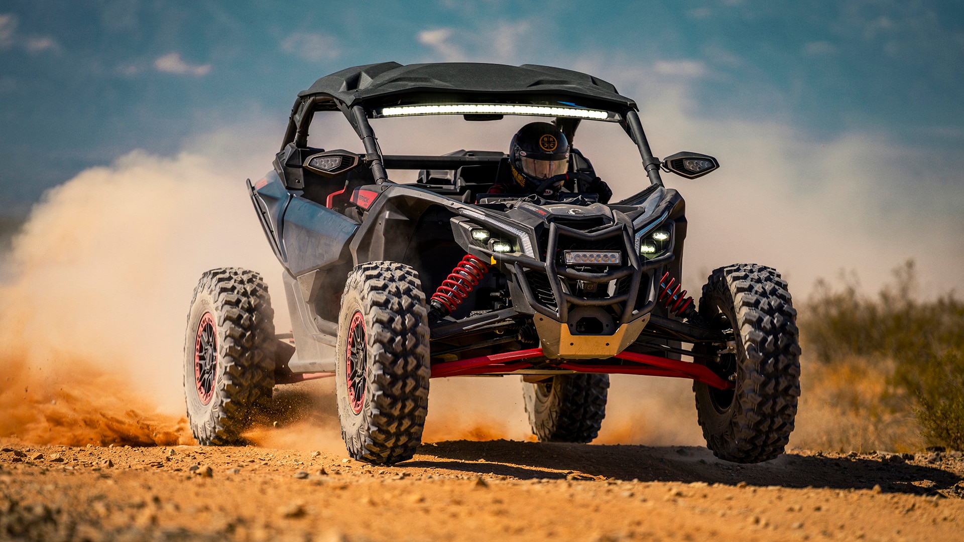 A 2026 side-by-side Maverick X3 X RS rolling through the desert, leaving a trail of dust behind it