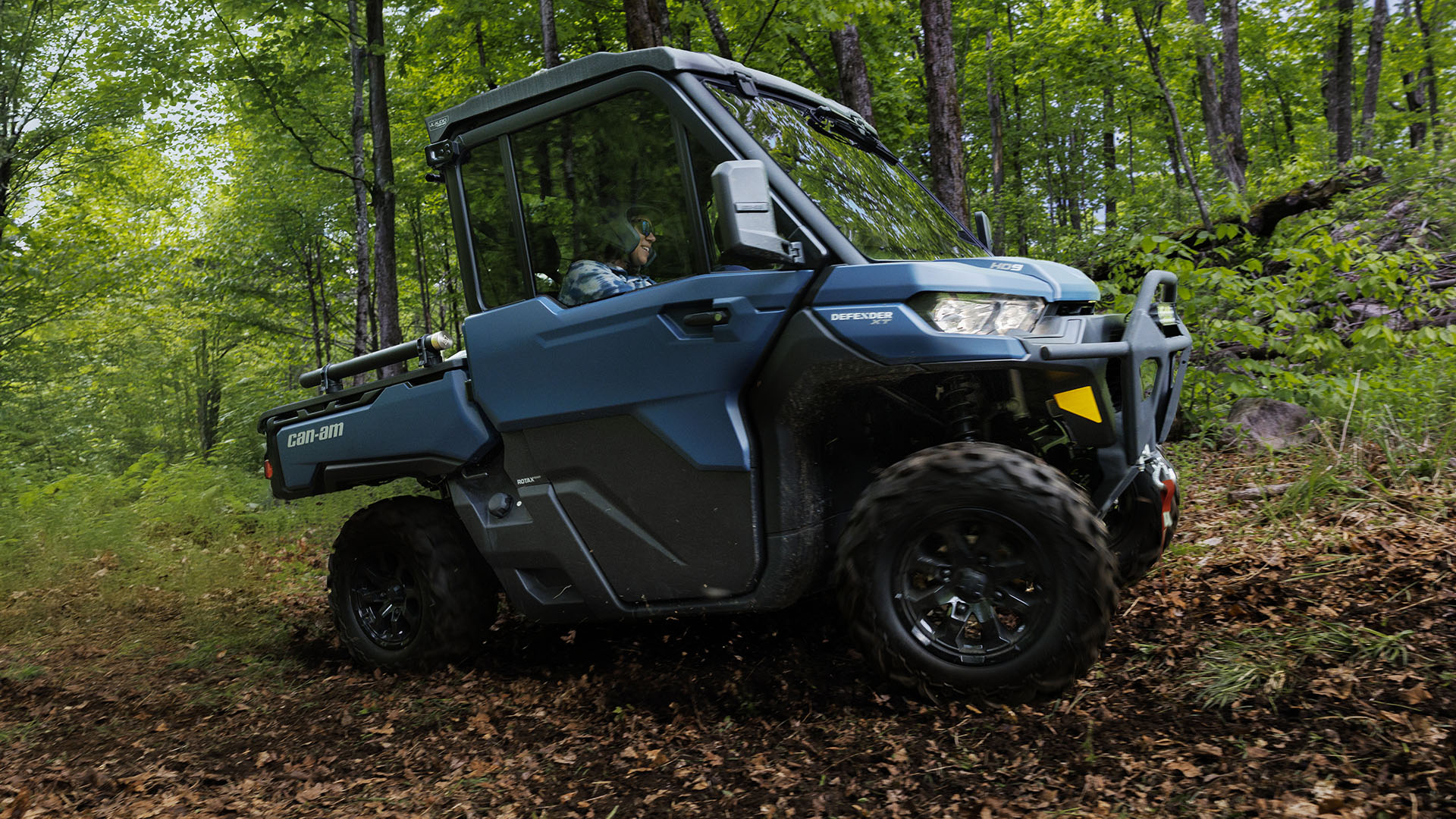 2 people in the 2026 Can-Am Defender XT HD9 side-by-side on a forest road
