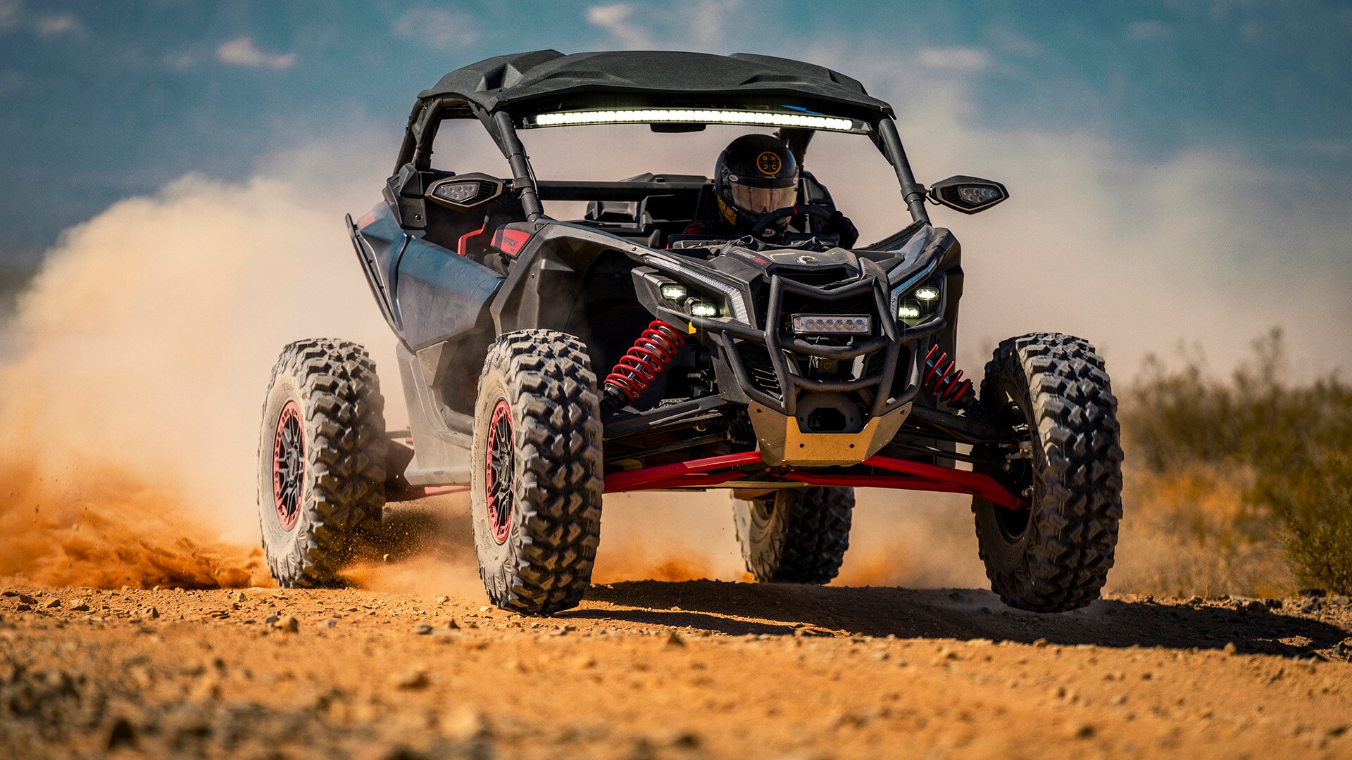 Un SxS Maverick X RS 2026 filant à travers le désert, laissant derrière lui un nuage de poussière.