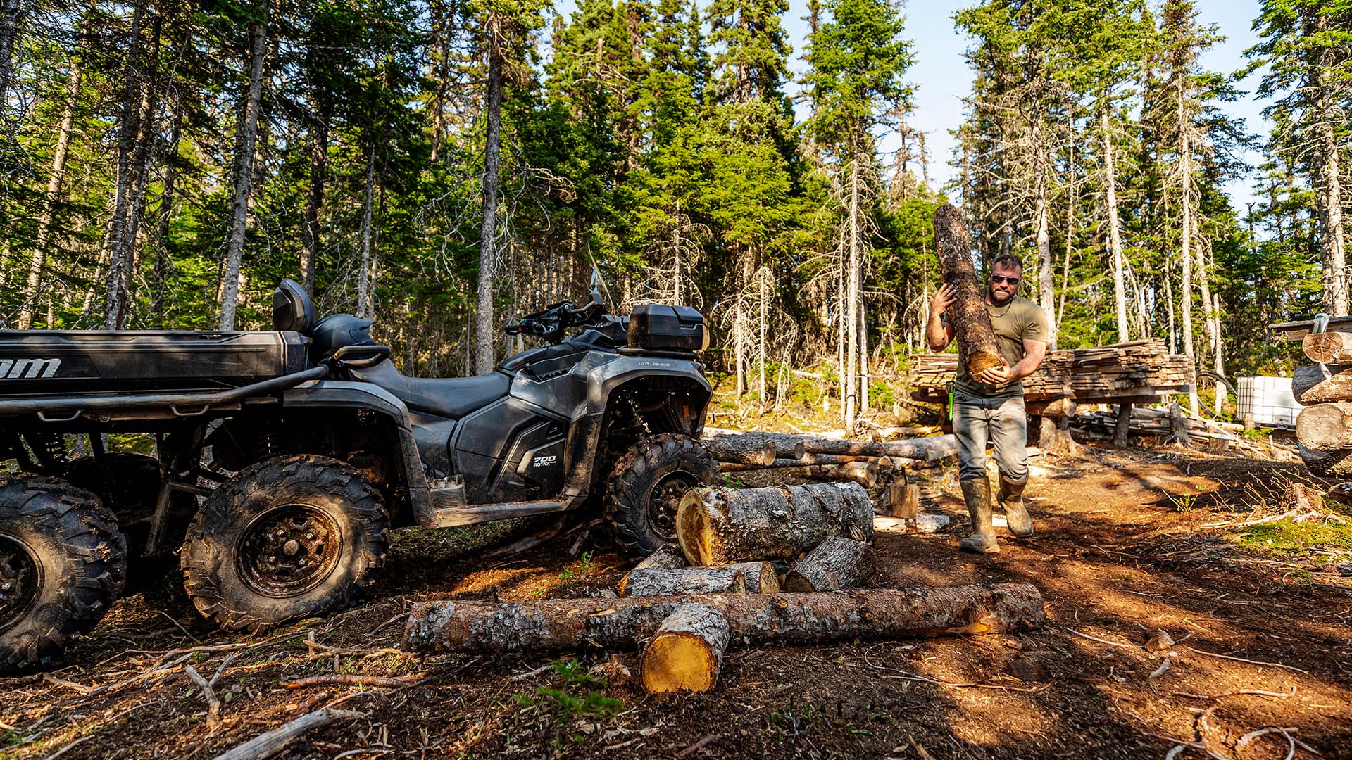 Man carrying wood near his Can-Am Outlander 6x6 in the forest