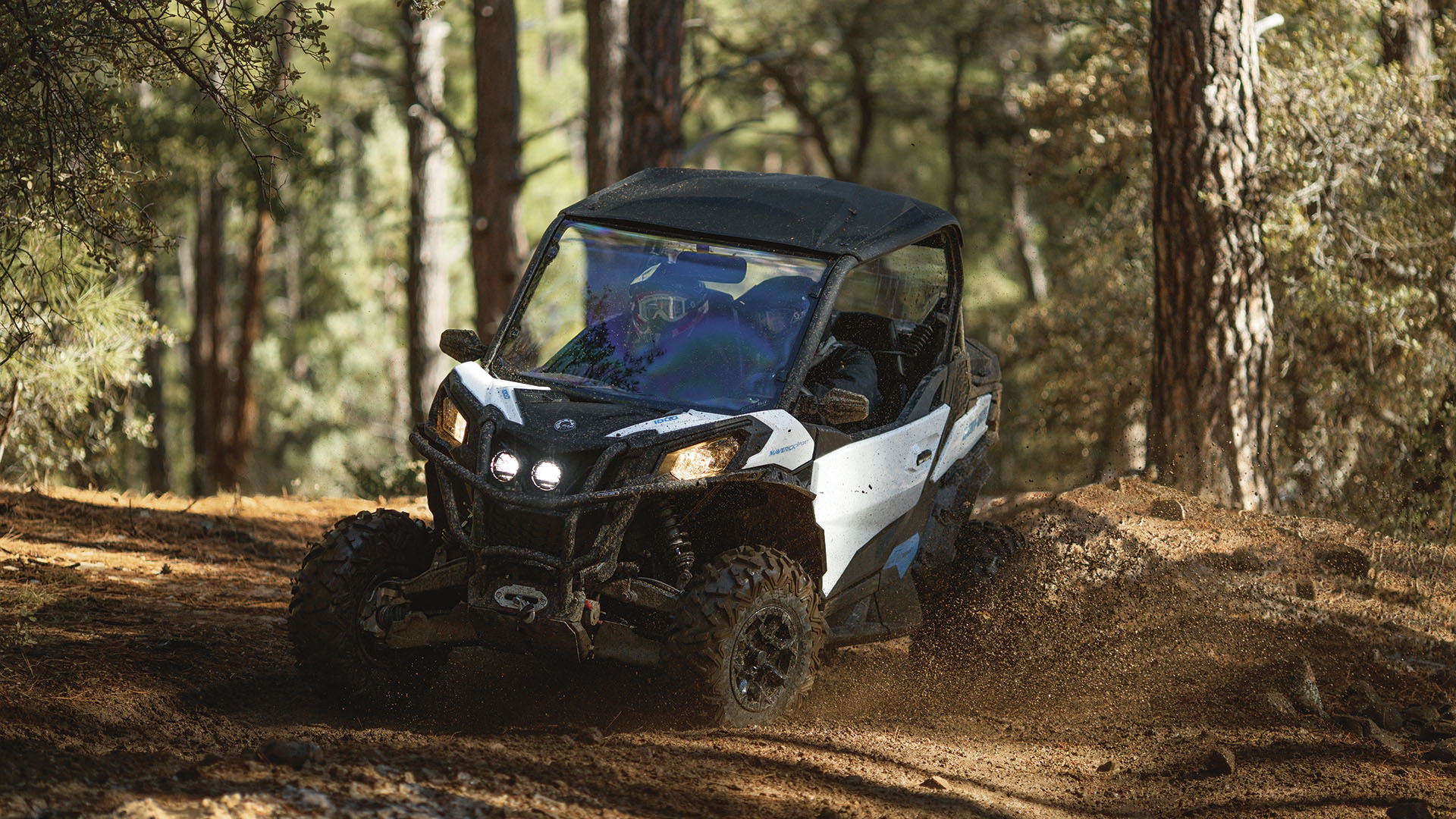 Can-Am Maverick Trail side-by-side rijdt op een onverharde weg midden in een bos