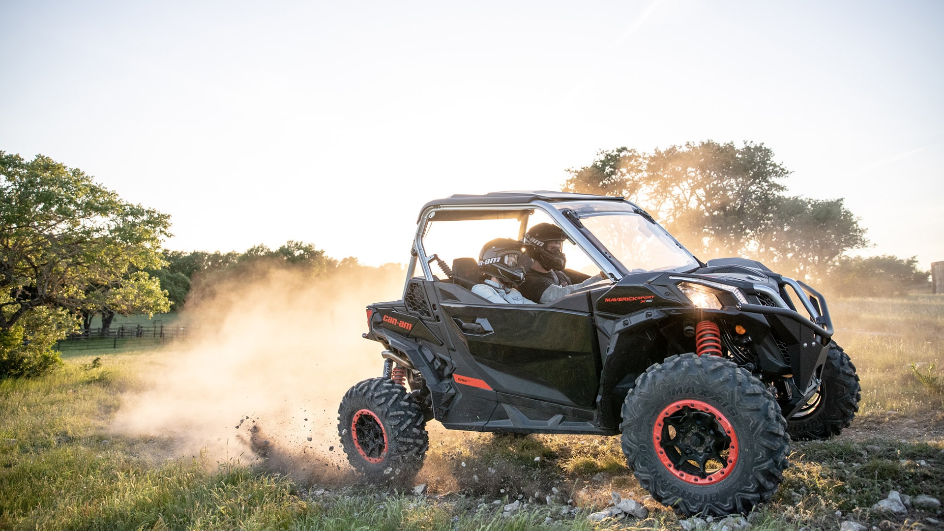 Two riders in a Can-Am Maverick Sport leaving a trail of dust behind them
